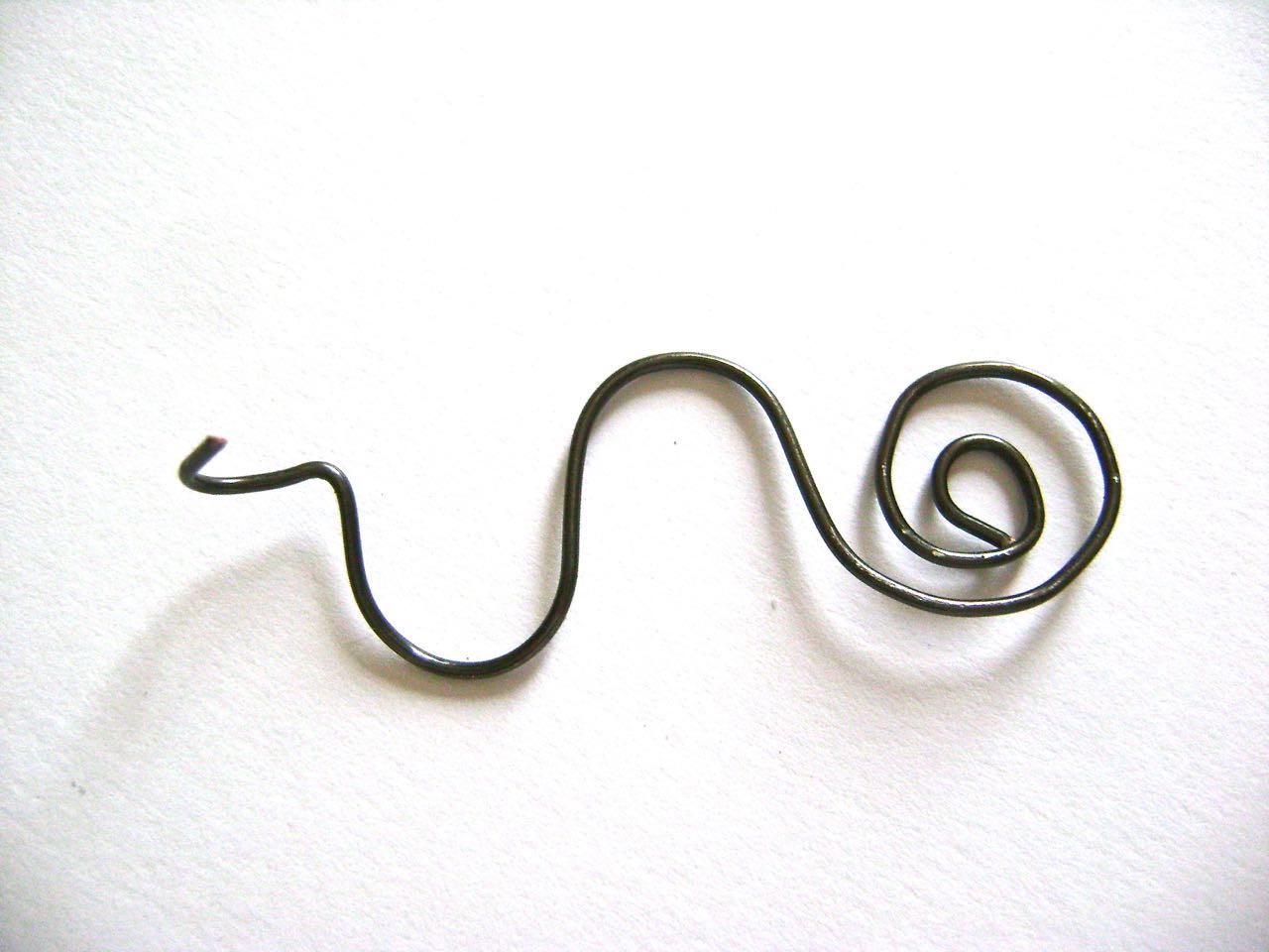 step 10 - Cut a piece of black wire to measure 4”. Roll one end into a spiral using flat nose pliers. Wrap the remainder of the wire around a magic marker twice in opposite directions, smoothing the wire over the marker in an “S” shape. Make a 90 degree angle in the wire then curl the end into a loop with round nose pliers. Put the wire through the hole in the top of the boot before closing the loop. 