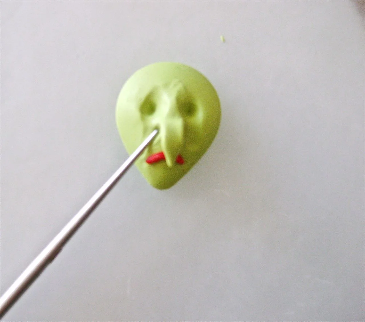 step 4 - Begin refining the face with an Etch n’ Pearl tool by creating lines between the nose and the mouth. Roll bits of green to create eyelids over the sockets. 