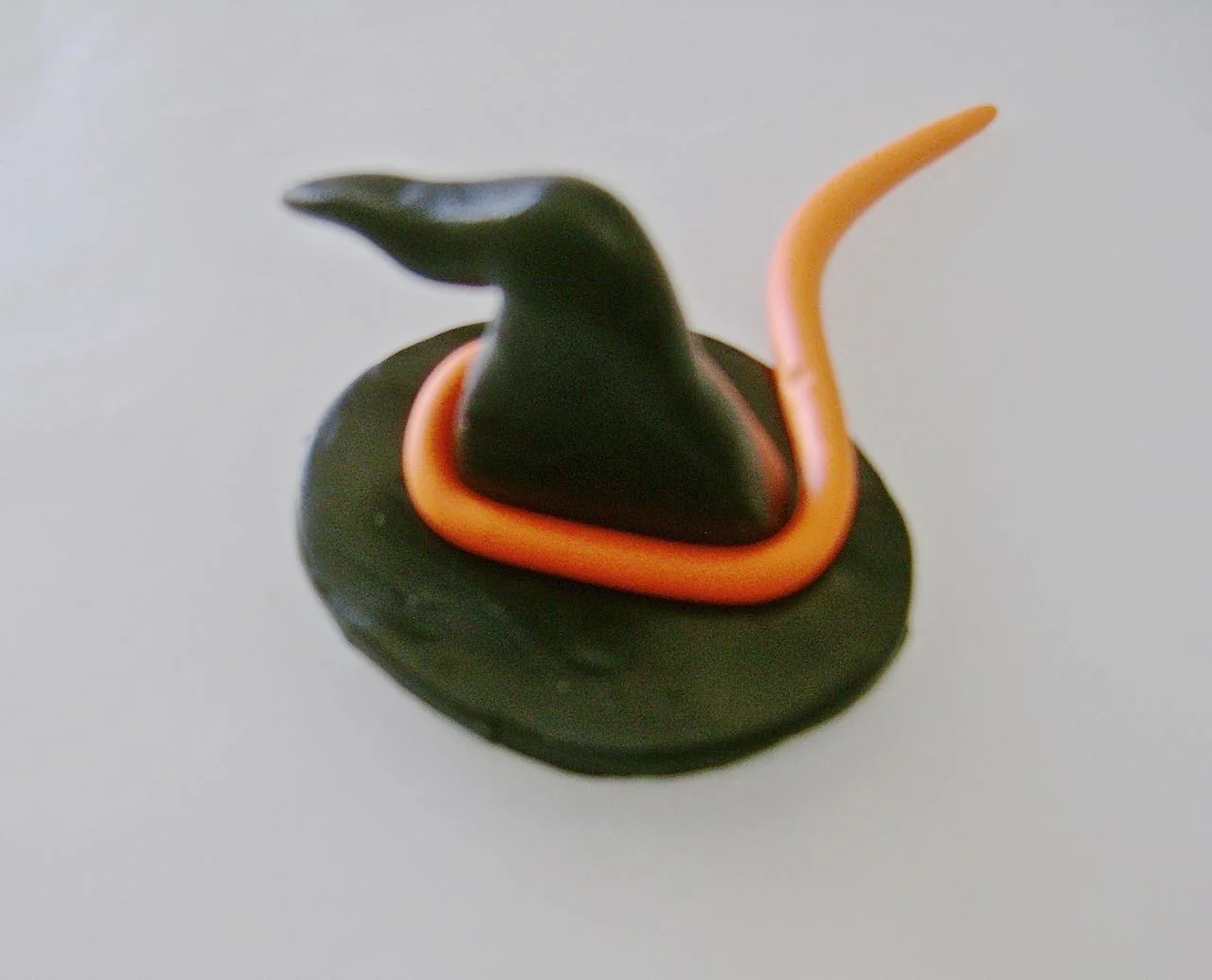 step 9 - Roll orange clay to create a hat band. Press the witch’s head into the hat and pull the brim down in front slightly.