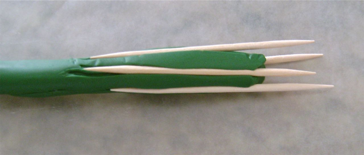 step 8 - Roll green clay into a tube. Press toothpicks into it and roll to leave the pick impressions. Use a slicer blade to cut the top and bottom of the Pumpkin stem. Pinch one end of the stem between your thumb and index finger to shape the bottom of the stem. Press it to the center top of the pumpkin.