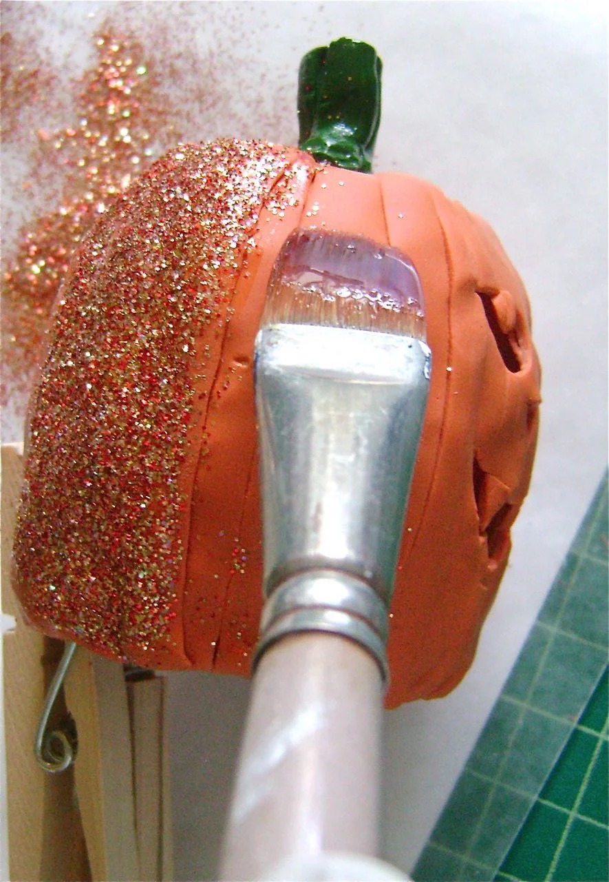 step 13 - Brush glaze on the pumpkin and sprinkle with orange glitter. Shake off excess. Work in sections. A clothespin is a convenient way to handle the clay during this step. When the glaze is dry and no more glitter can be shaken off, use the brush to paint over the glitter to keep it from shedding.
