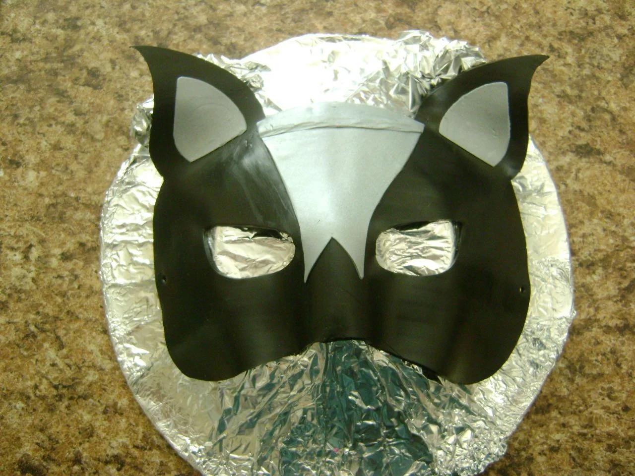 step 9 - Drape the clay over the bowl with the cork in the center of the mask and the bottom end of the cork aligned with the bottom end of the mask. Lightly press against the side of the clay nose with another cork to shape the nose. Ball up some foil and place it under each ear to make them curve forward.