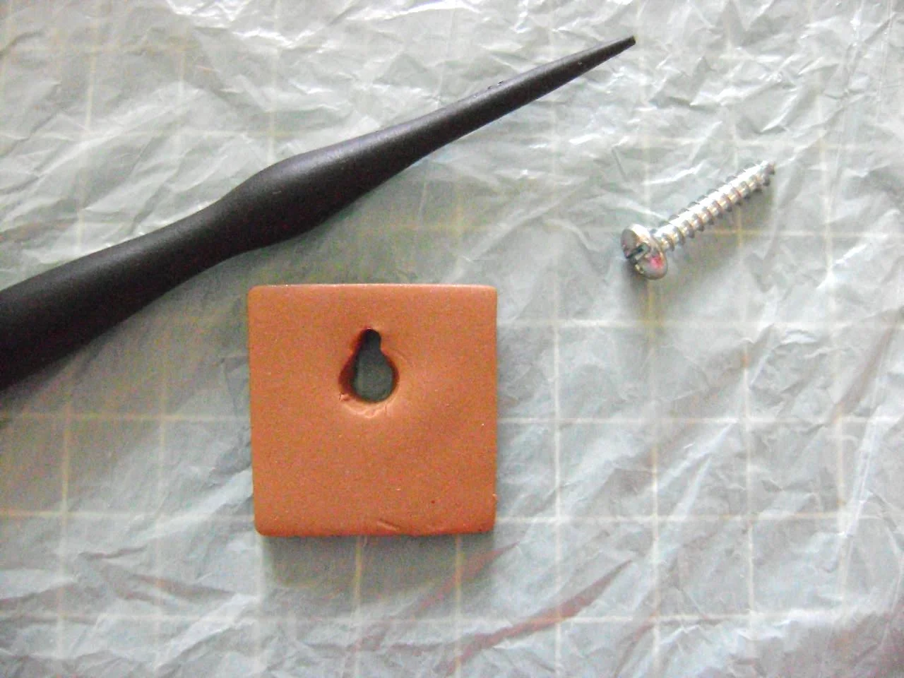 step 4 - Cut a thick piece of clay measuring about 2” square. With clay shaping tools, make a hole to accommodate the size nail or screw you will be using to hang the sconce.