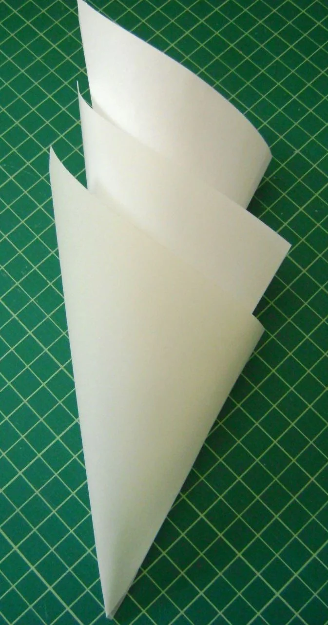 step 6 - Cut three cones, one from a stencil blank, which will provide support; one from regular paper, which will diffuse the lights; and one from eggshell toned vellum paper for aesthetics. Each cone should measure 6.50” square. One cone at a time, place the side edges together and join them with transparent tape. Place the cones inside each other with the vellum cone on the outside. If one cone is slightly longer than another when stacked, trim it from the top edge.