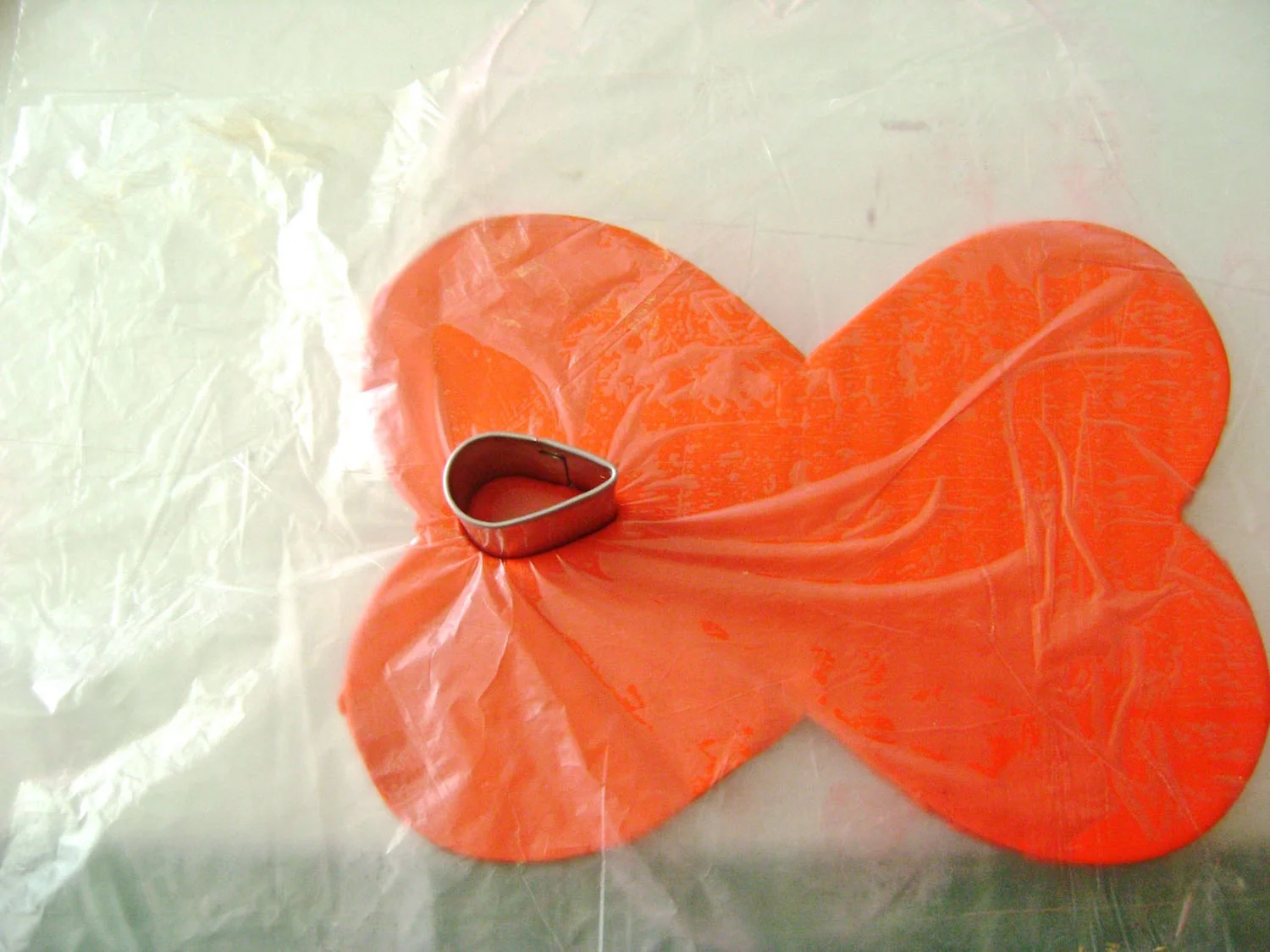 step 3 - Cover the cuff with plastic wrap. With a teardrop shaped cutter, press down to cut a hole in the clay on the left side of the cuff. Position the cutter on the right side and create an identical cut.