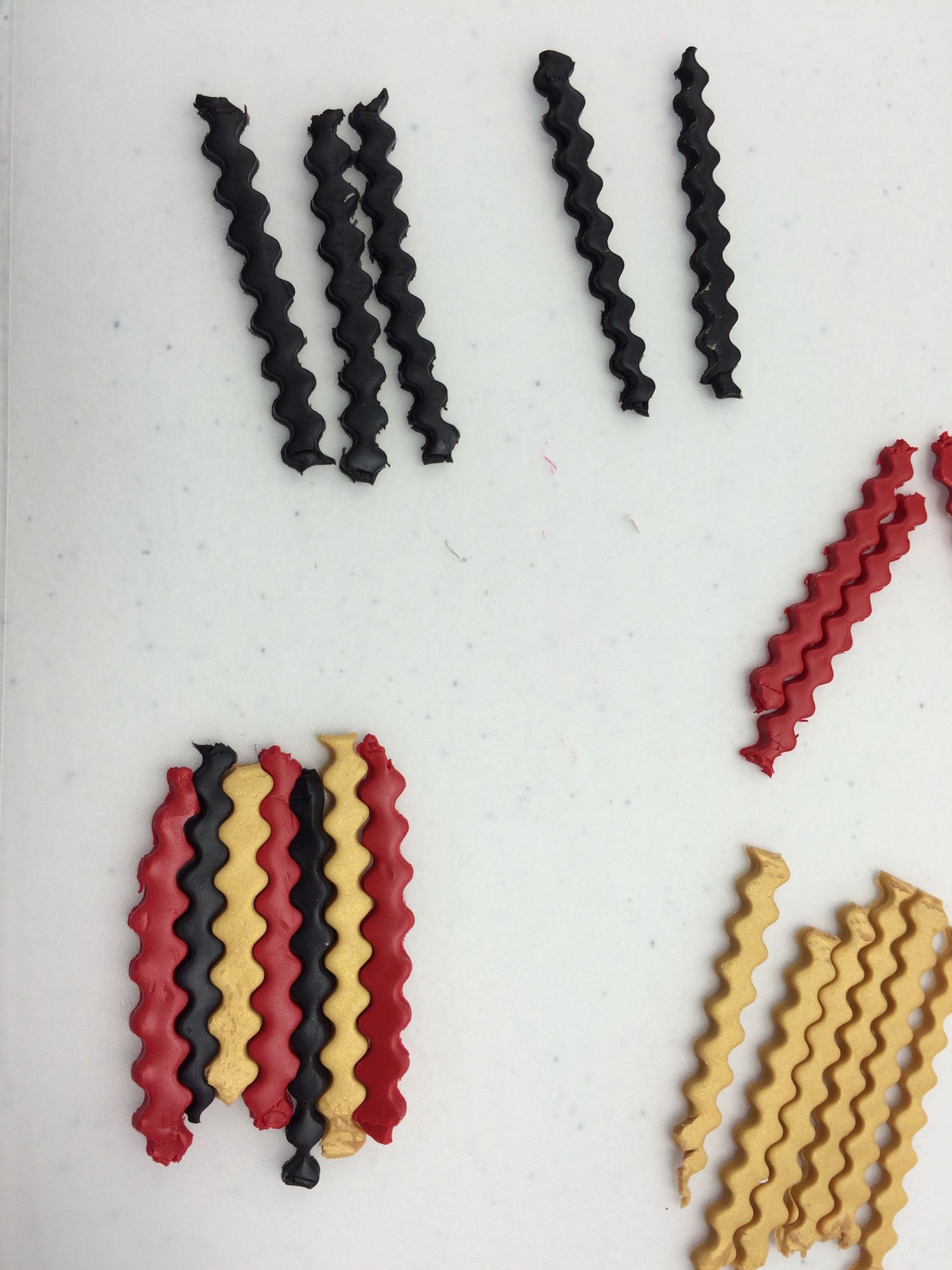 step 3 - Roll out the remaining clay colors on the #2 setting. Use a wave blade to cut 1/8” strips. Include the gold leaf clay which is not shown in this photo. Fit them together like a puzzle alternating red, gold, black and gold leaf. Press on them so they stay together.