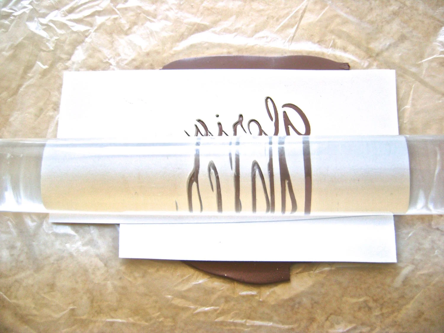 step 4 - Place the card stock onto the clay with the unreadable side facing up. Either run them together through the conditioning machine on the widest setting, or roll over the signature with an acrylic roller until the clay has risen up to the top layer of the card stock. Carefully peel the card stock away from the clay.