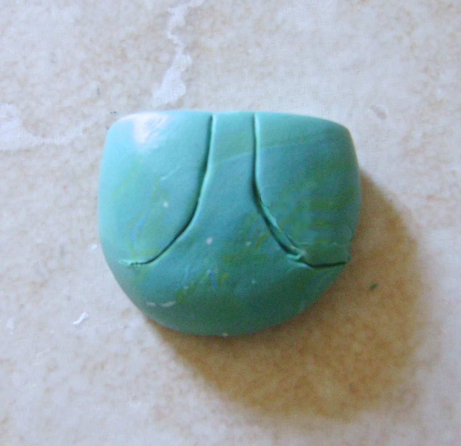 step 1 - Roll 1 oz. of conditioned blue clay in your palms to form a sphere approximately 1.50” around. Squash the ball slightly. The mound should not be flatter than .75”. With a blade, cut off one rounded end. Cut the center face shape.