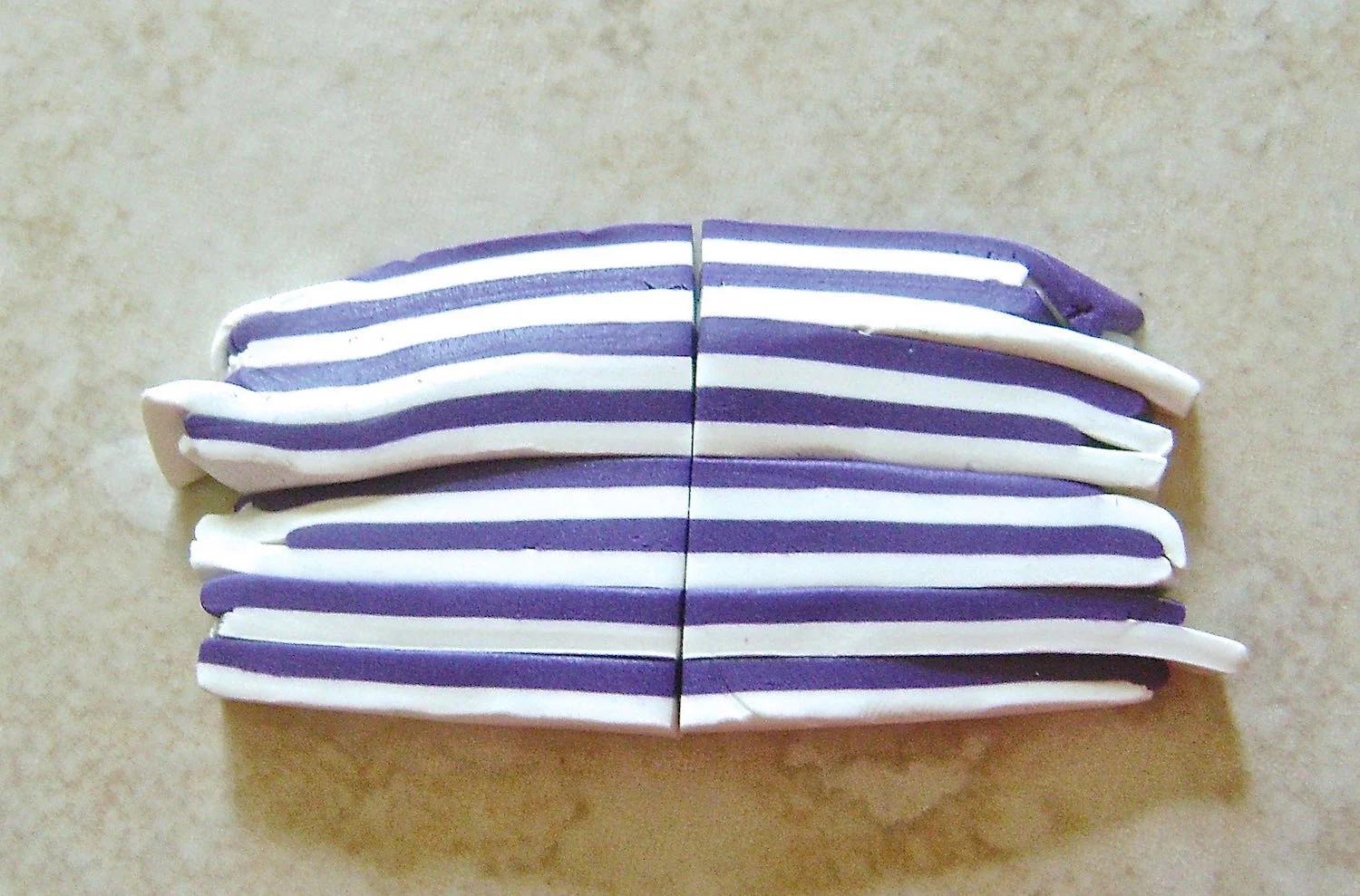 step 6 - Cut a small amount of purple and white clay into strips stacking and alternating them. Continue cutting in half and stacking until you have a thin striped strip to fit at the base of the hat.