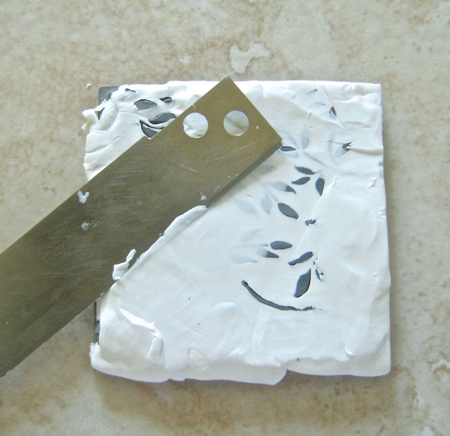 step 1 - Roll white clay into small balls in your hands. Press the balls into the surface of a rubber stamp. Rubber stamps should be removed from wood blocks for this technique because the rubber must be rolled off the clay later. Use a tissue blade to cleanly skim the clay off the entire surface of the rubber.