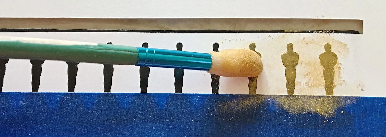 step 4 - Place painters tape at the base of the statues. Use a sponge applicator to apply gold powder to the exposed images.