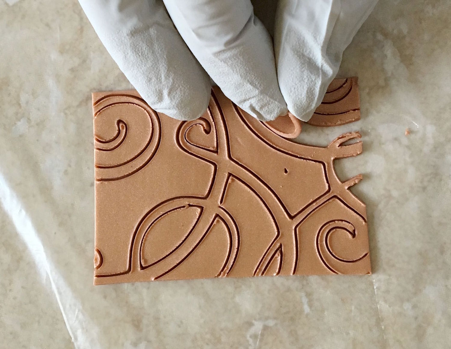 step 8 - Flip the clay onto a clean sheet of deli film. Curio Users peel off the freezer paper. Craft Knife Users peel off the old deli film. Remove negative clay pieces from the scroll design.