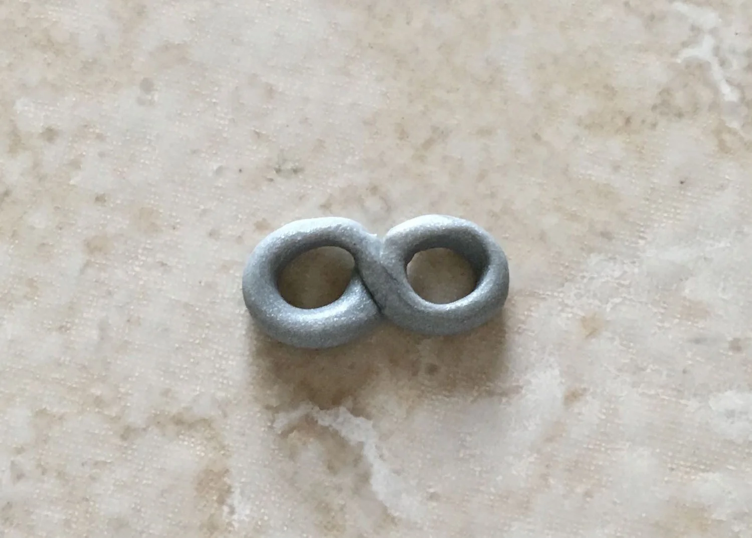 step 5 - Roll a thin piece of silver clay on the work surface. Create a figure eight to act as the goggles.