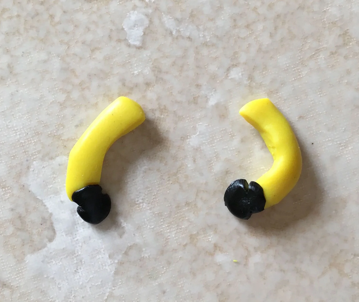 step 11 - Roll two thin tubes of yellow clay for the arms and bend them at the elbow. Attach tiny globs of black clay to serve as work gloves.