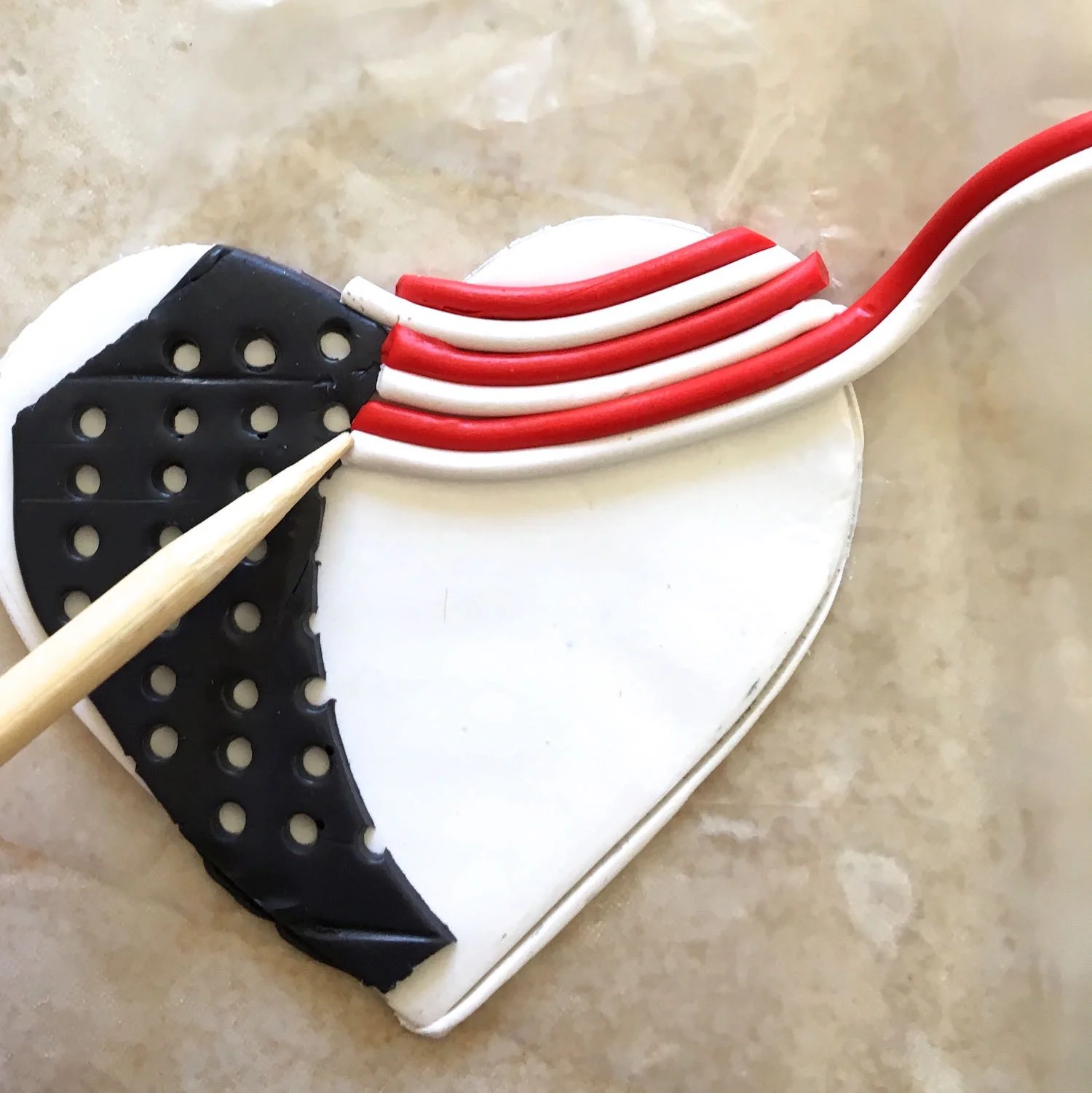 step 7 - Add the strands to the heart, alternating between red and white. The edges should be placed flush against the edge of the blue clay. Curve the strands slightly. Fill the remaining white space.