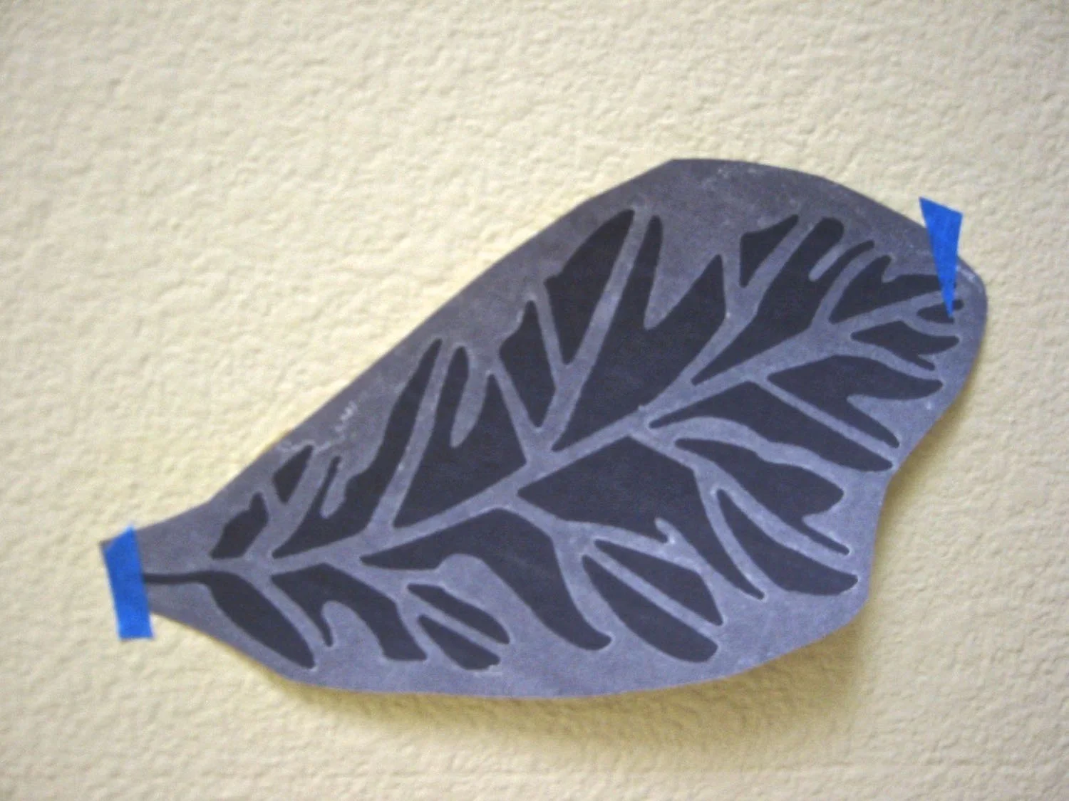 step 1 - Make several photocopies of your stencil with color paper behind it to show the shape. Roughly cut out the copied leaves. With painter’s tape, temporarily attach the leaves on the wall in different positions to get an idea of where you want your final design placed. Also try adding or subtracting pieces to determine how many you will want. Once you’ve made those decisions, you’re ready to begin stenciling. 