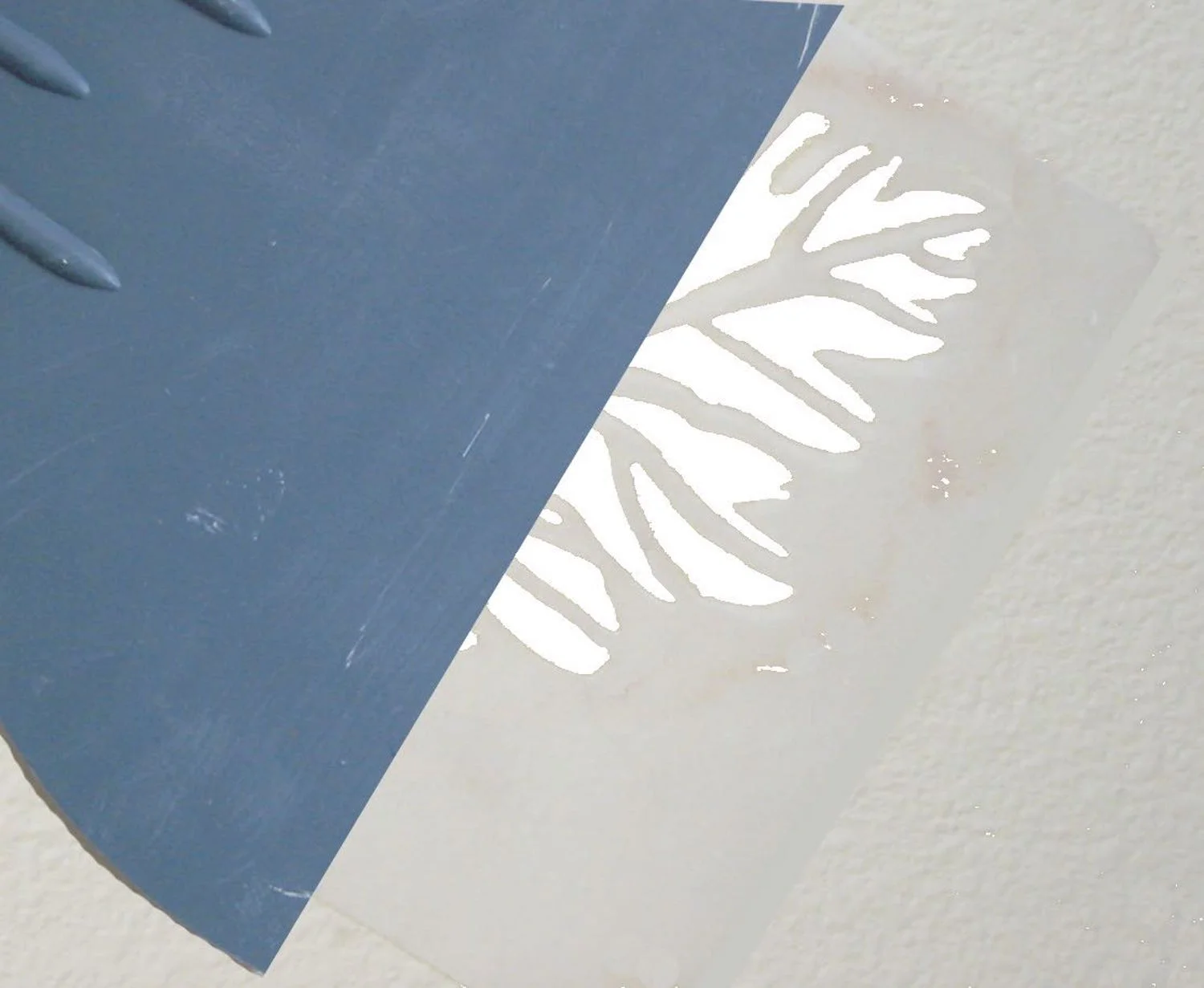 step 4 - Squirt tub caulking into a shallow, disposable container. With a putty knife, apply the caulking to the open areas of the stencil. When the open areas are covered, gently glide a straight edge over the entire stencil with one pass, to create a uniform surface. Don’t dig down with your tool or too much caulking will be wiped away which will create a less dimensional leaf. 