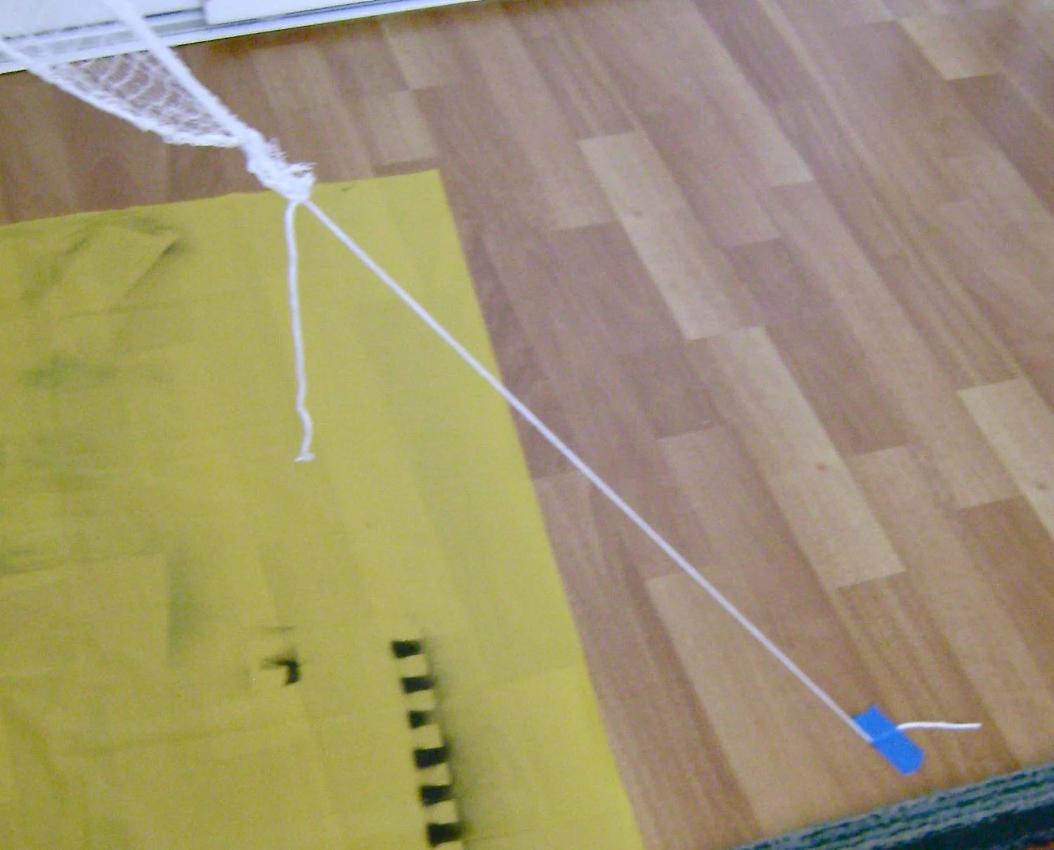 step 7 - Tie a piece of string or yarn to eight corners of the cloth. The string/yarn should be long enough to reach the floor or a nearby stationary object. Using painters tape, secure the string/yarn with the cloth stretched out in different directions.
