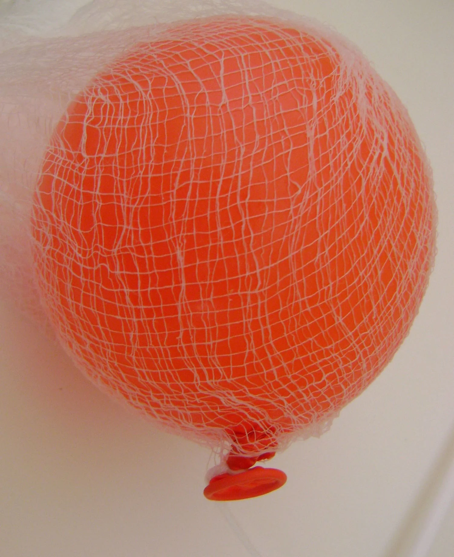 step 2 - Partially inflate a balloon so that it is about the size of the top of a water bottle. Make a tiny hole in the center of wet, starched cloth and push the balloon knot through it. Attach a string for hanging. 