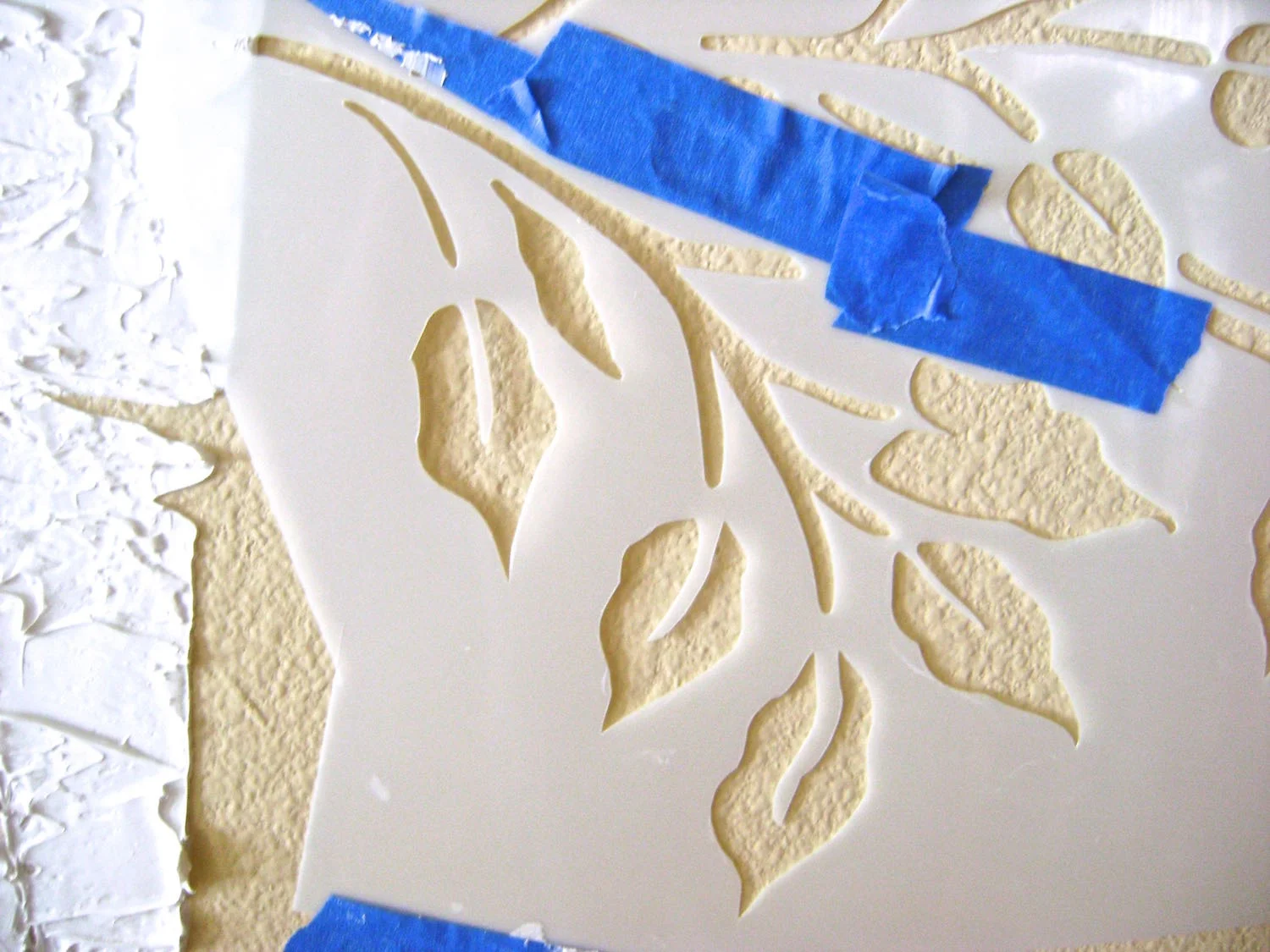 step 8 - When adding leaves, keep in mind that you don’t have to use the entire stencil as is. Apply painters tape to close off openings in the stencil to create a smaller grouping. Also flip the stencil over to create leaves that bend in a different direction. Texture the leaves with the knife just as you did the trunks.