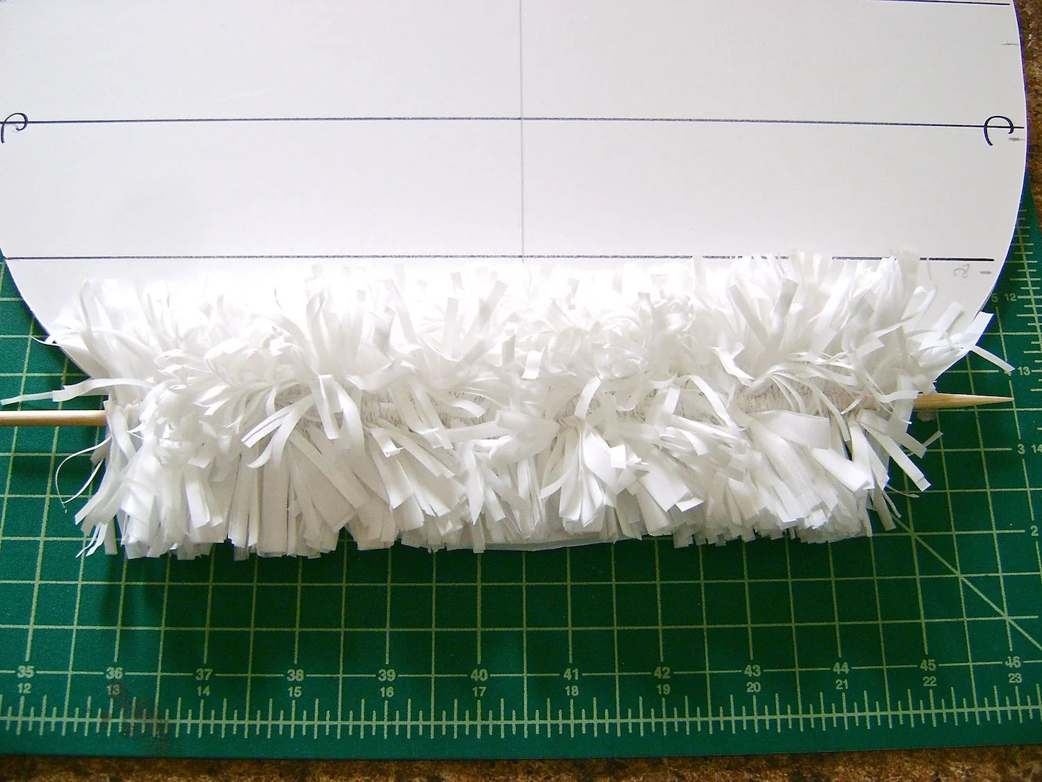 step 7 - Apply a generous amount of hot glue along the bottom line on the egg. Place the white gathered set on the line making sure the skewer is lined up with the pencil line. When the glue is cool and set, slide out the skewer. Gather the next set which will be white, followed by a color set, two whites, and another color set. Finish the rest of the egg with white sets.