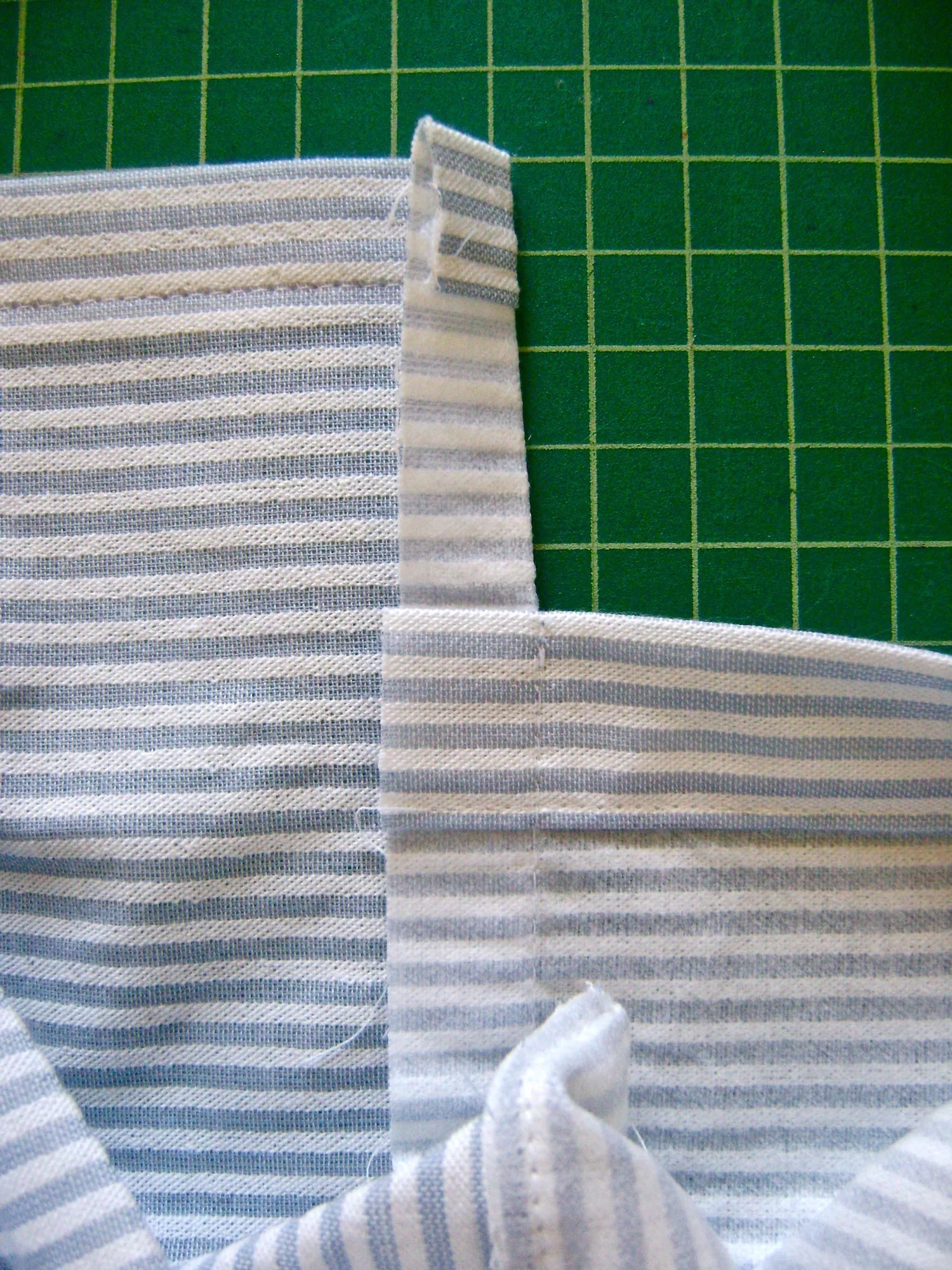 step 11 - Press the side seams to the pocket back. Trim the seam allowance to one quarter inch. Turn the pocket right side out. Top stitch across the bottom 3/8” from edge.