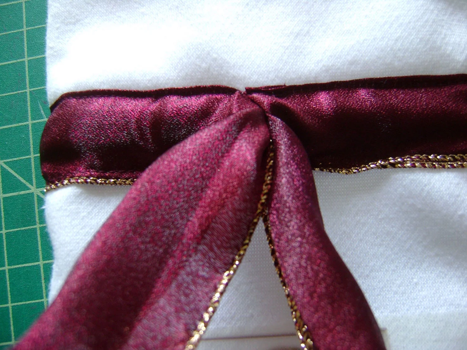 step 12 - Bring the safety pin out the center front. Put the bottle in the bag and tie the two ribbons together then into a bow. Cut off excess ribbon.