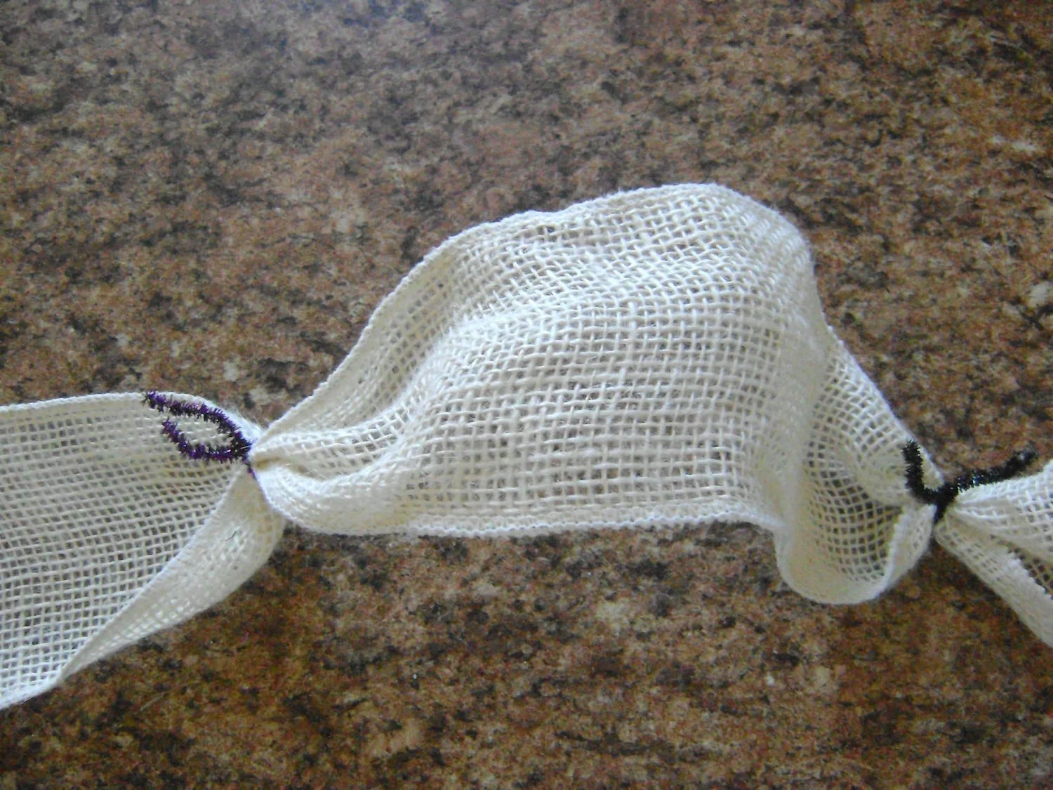 step 6 - Twist a pipe cleaner, jewelry wire, or floral wire around the burlap ribbon ten inches from the end. Move across the ribbon attaching pipe cleaners every ten inches until you have eight. Cut off the excess leaving a 10 tail on the end. Hot glue the edge to prevent it from fraying.