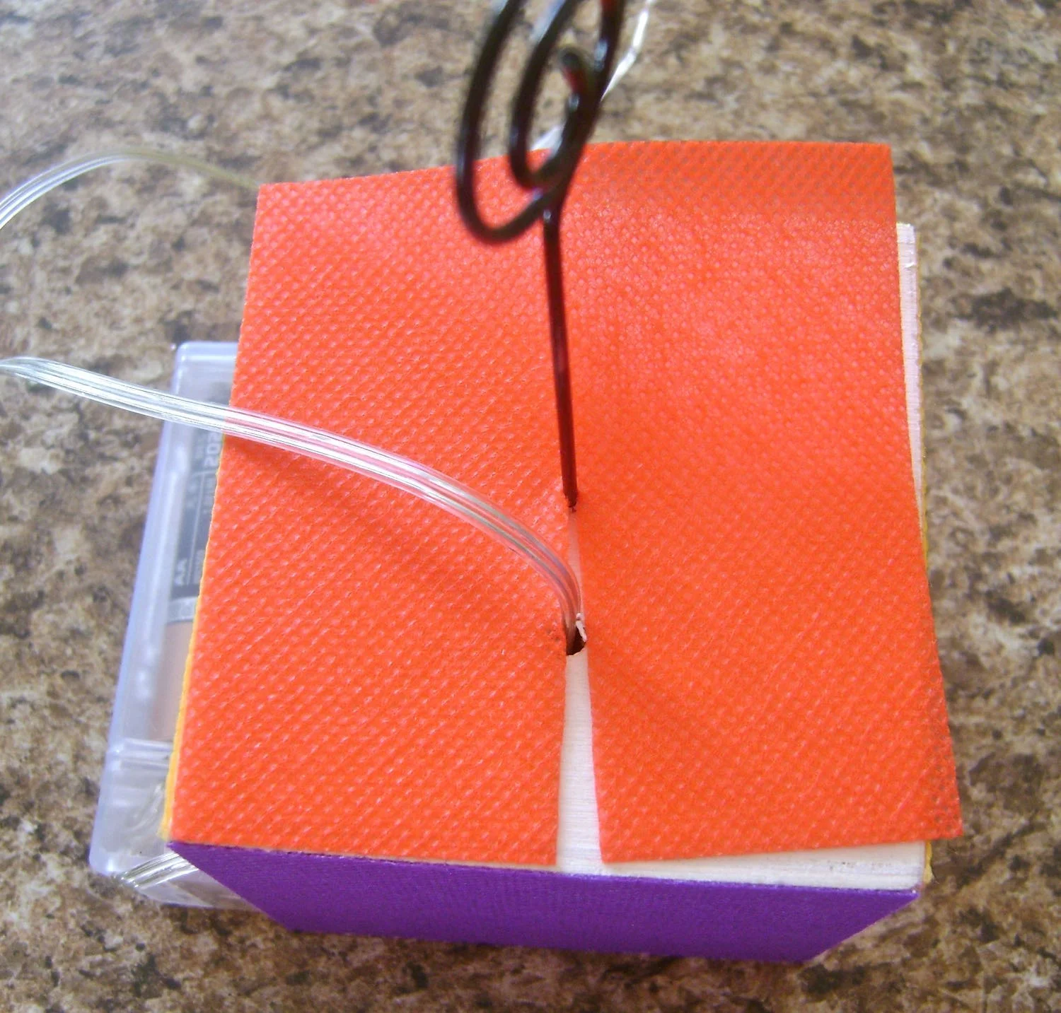 step 6 - Apply a gold “X” on three of the fabric squares with Beads In A Bottle. When dry, attach silver stars in the center with hot glue. Attach the gold “X” squares to the front and two sides of the cube with the glue stick. Glue a plain square to the bottom of the cube. Make a cut halfway through the remaining square and slip it around the light string and photo wire on the cube top. Bring the slice together and glue in place.