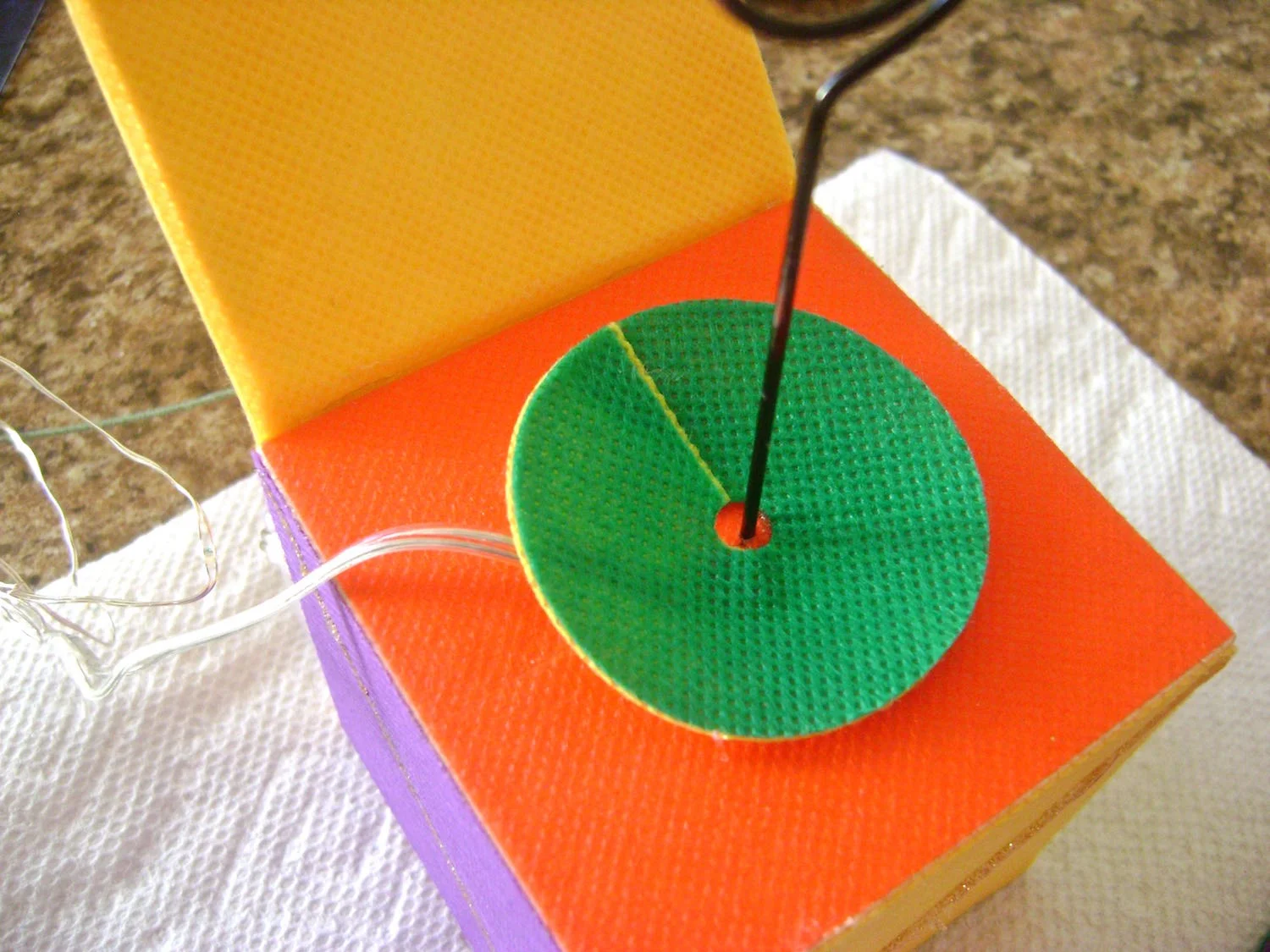 step 11 - Slip each disc around the photo cube wire. Overlap the ends until the disc curves upward or down and hot glue the ends together. Repeat with all seven discs stacking them on the wire.