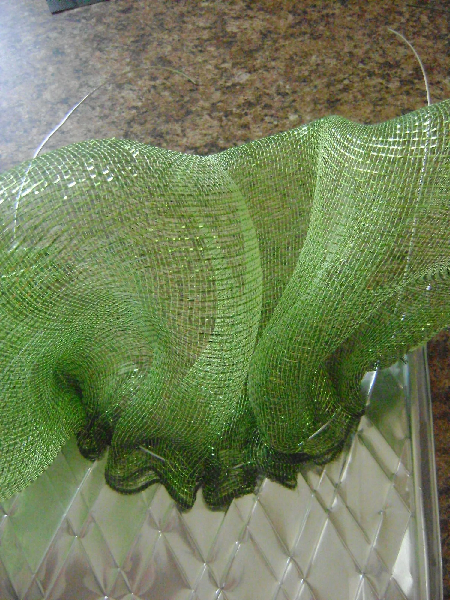 step 6 - Gather the mesh in the center of the wire leaving 9" leads on each end for the hanger. Apply a heavy glob of hot glue on the mesh ends to keep them from slipping across the wire. Align the wired mesh with the curve of the embossed foil. Hot glue the mesh to the foil starting in the center and working out to the edges.
