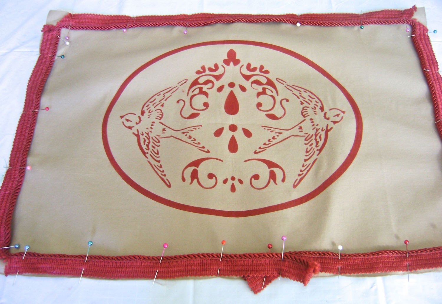 step 10 - Pin the cord trim to the painted fabric with the trim's raw edge matched to the raw edge of the fabric. Overlap the trim at the center bottom. Slash the trim at the corners so it will lay flat.