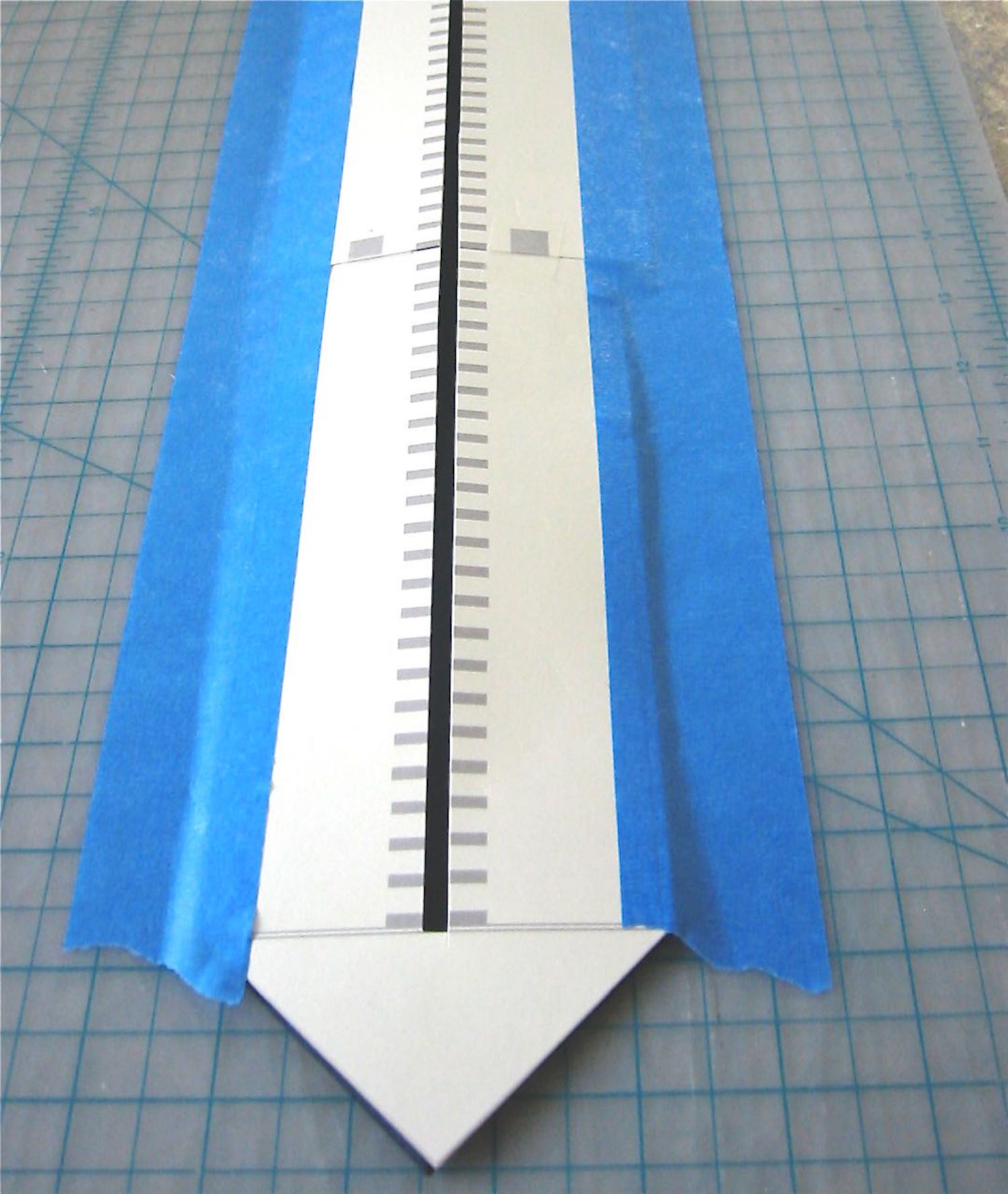 step 2 - Place a hard work surface (like a cutting board), on an ironing board. Match up the large angled edge of the tie with the angled edge of the template, making sure the center of the template matches the center of the tie. Use painter’s tape to secure only the very outer edges of the template and tie to the work surface so it doesn’t shift.