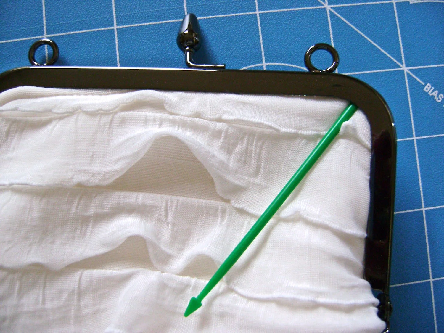 step 13 - Attach the purse to the frame. Starting with the top center of the purse and working out to the sides, push the fabric edges into the frame’s groove. Use a tool like a plastic pick to push the edges into the corners. Let the adhesive set 24 hours. Attach the opposite side of the purse to the frame.