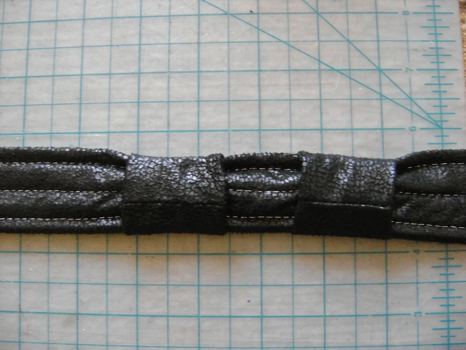 step 33 - Fold the strap end covers in half and sew the edges together. The finished piece should be 2.5” long. Slip both covers over the strap and move them to the center.