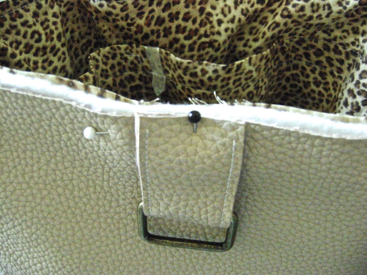 step 21 - Fold a tab in half and place the metal hardware in the fold. Pin two tabs on the front of the bag and two on the back, each tab 3.75" from the bag's side seams. Insert the lining/fleece section into the vinyl and sew around the top edge.