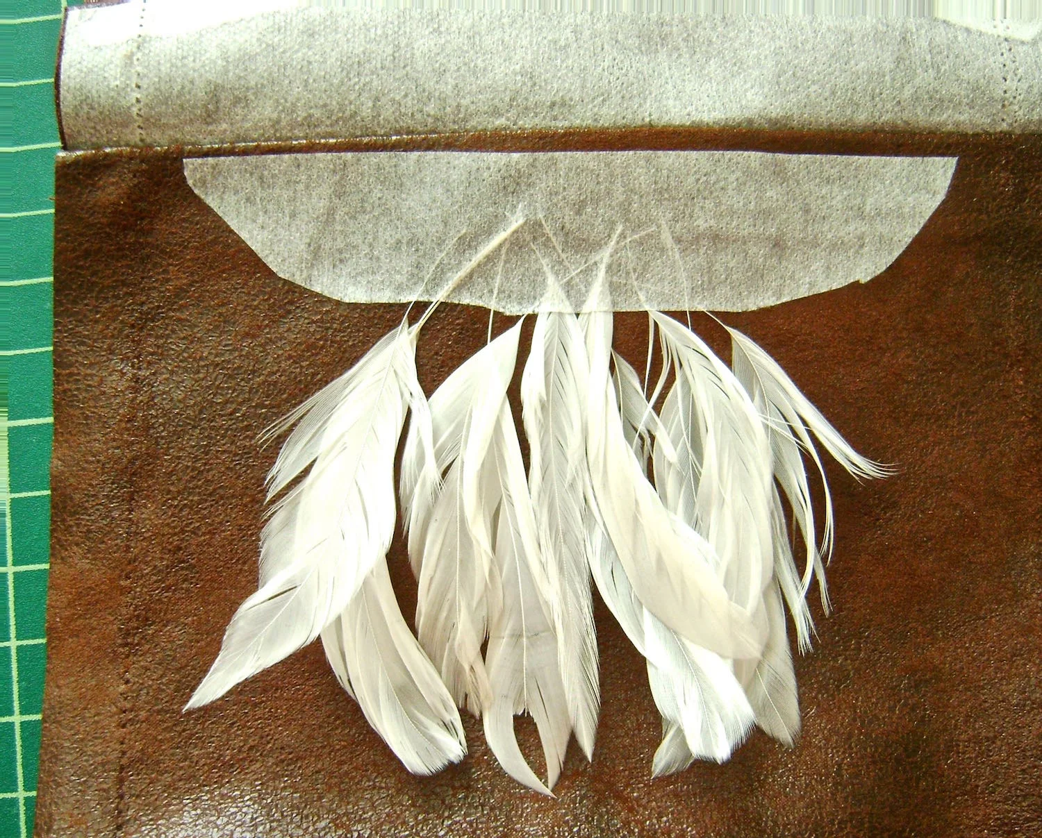 step 5 - Slip feathers under the interfacing centered on the front. Iron the interfacing to hold the feathers in place temporarily. Do not iron the feathers. Check to be sure the cover will hide the quills once sewed in place. Apply glue to the feather quills to hold them permanently. Allow the glue to dry. 