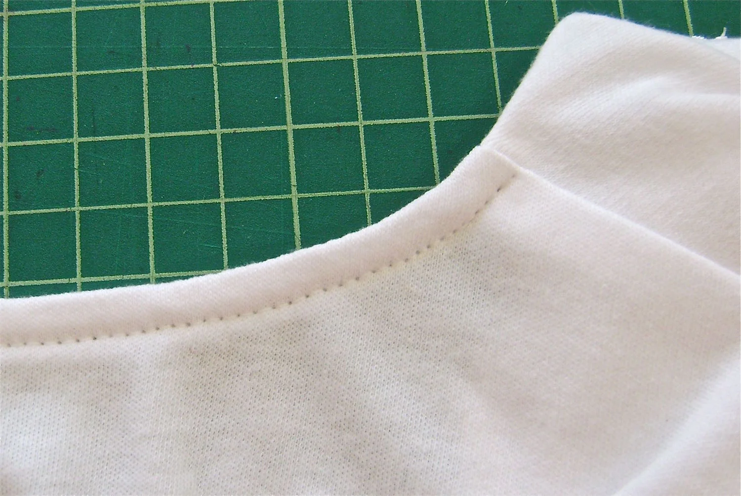 step 16 - Use a 5/8” seam to sew the band to the neck. Top stitch the allowance to the band then cut away excess bulk. Turn the band to the inside of the shirt and top stitch in place close to the folded edge, from shoulder to shoulder.