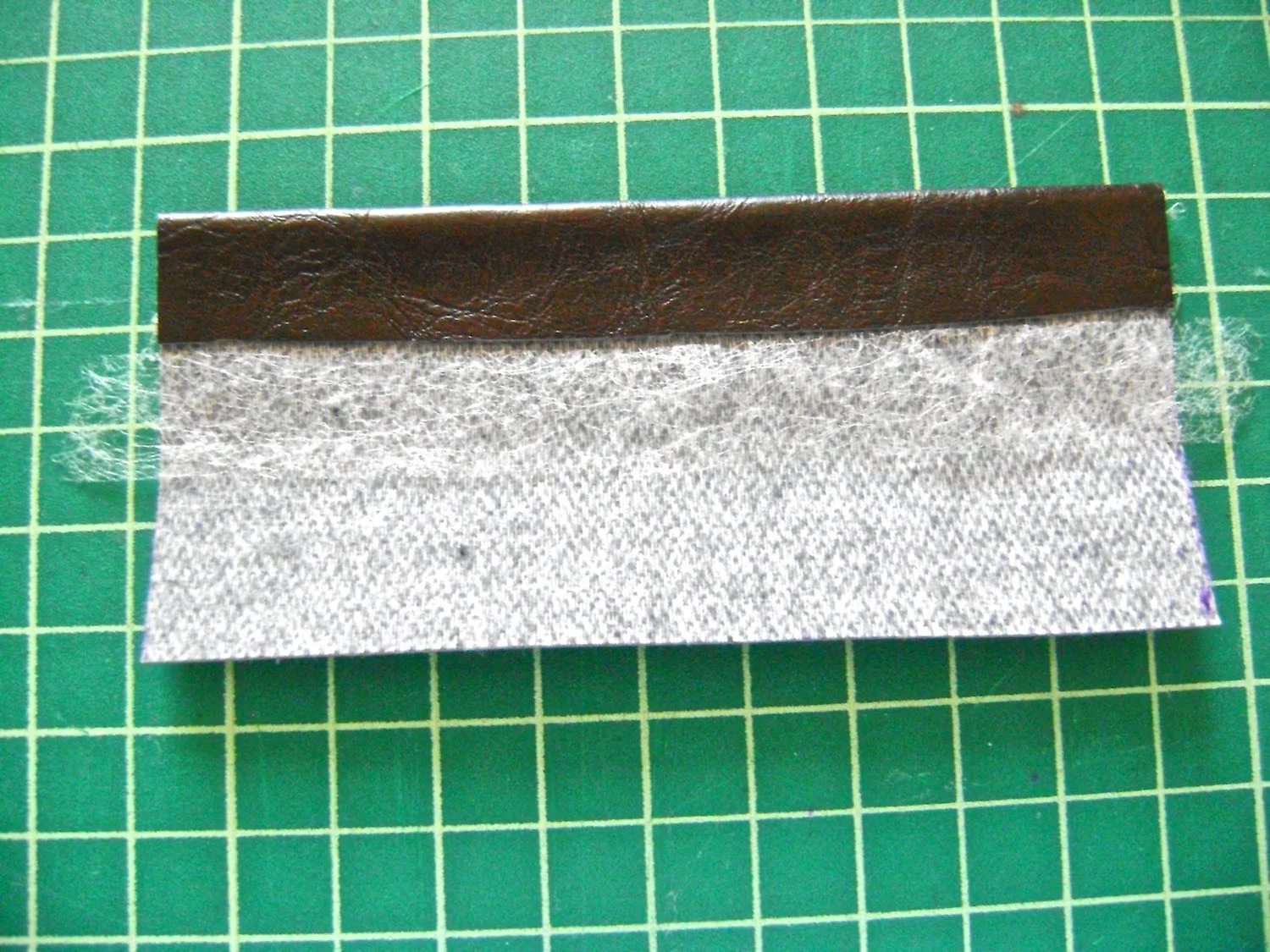 step 10 - Strap Tabs Center two strips of fusible tape side by side on the wrong side of the tabs. Fold the raw edges in to meet at the center and iron the vinyl with a pressing cloth to fuse the hems in place.