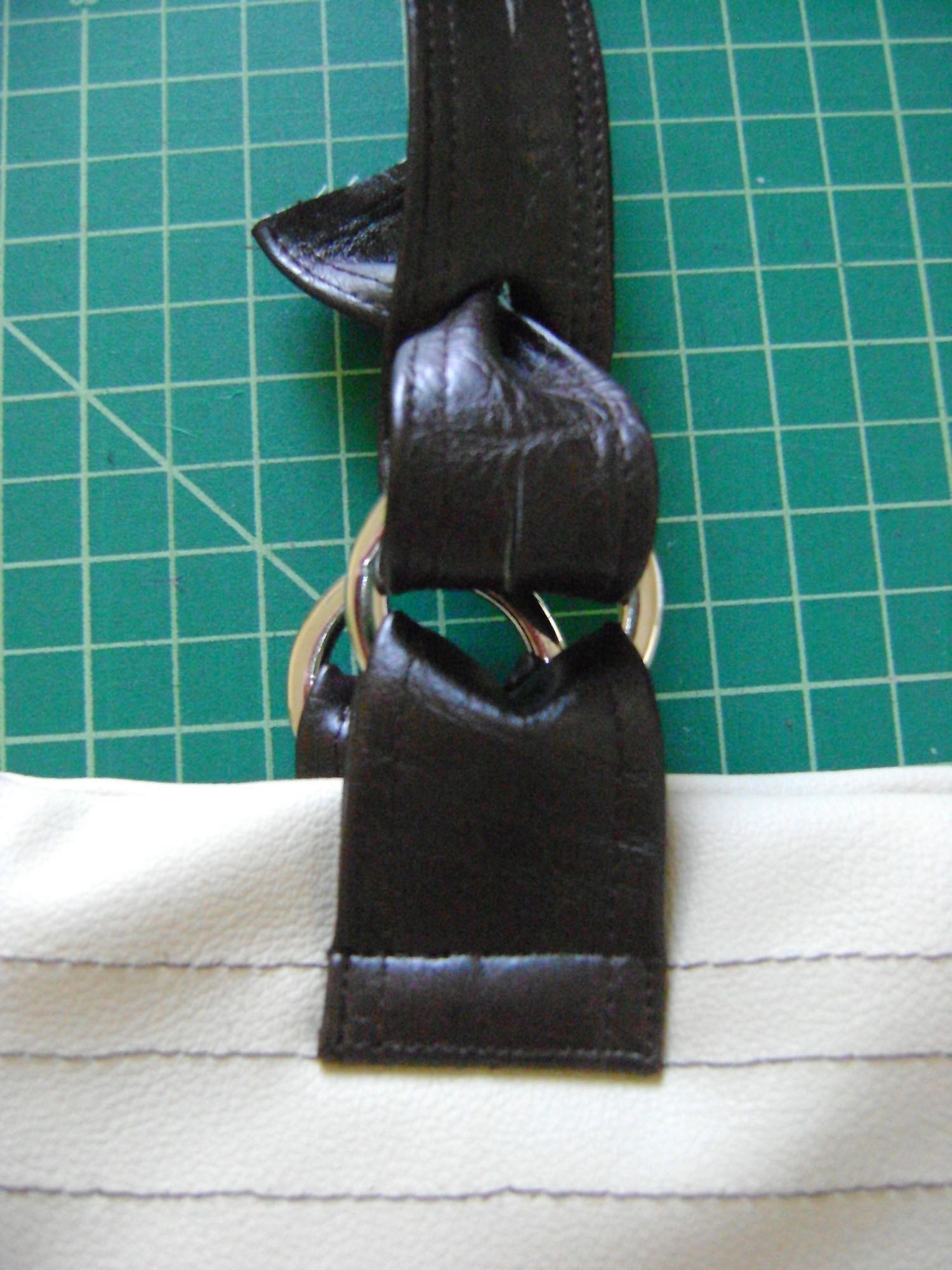 step 17 - Insert the hemmed end of the strap into the metal ring from back to front. Bring the end of the strap through slit one. 