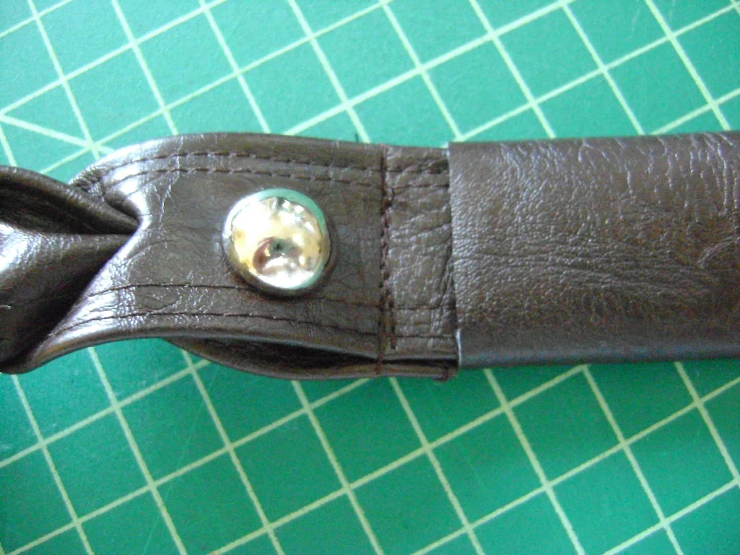 step 19 - Strap Covers Fold a cover in half to measure 2” by 4”. Sew a .50” seam with the right sides together. Turn the cover right side out. Slip it over the unfinished end of a strap and slide it close to the brad to hide the stitching that holds the two straps together. Turn the raw edges of the covers under on both sides so the cover measures 1.50” long. Apply E6000 glue under the covers to keep them from sliding up the strap.