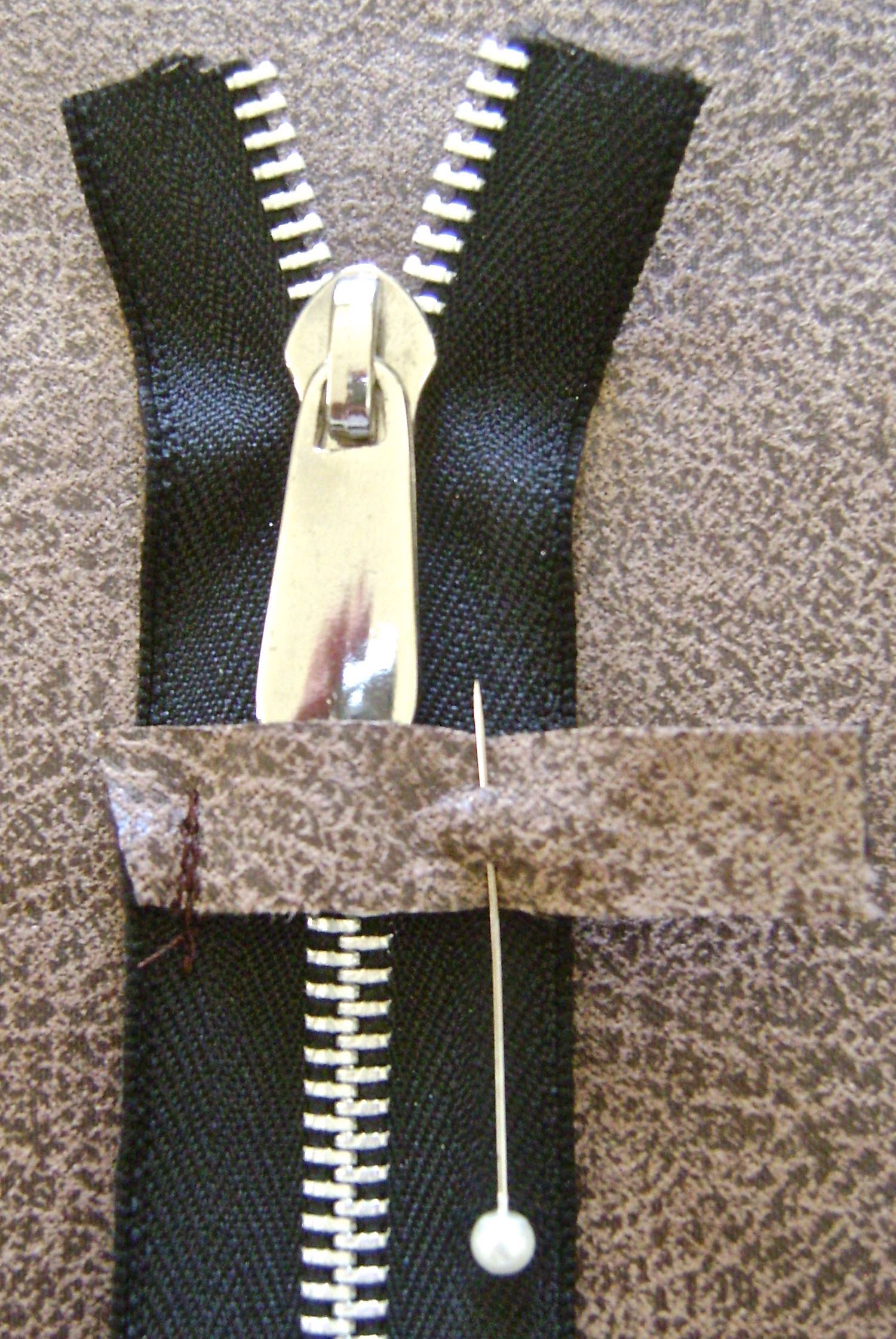step 8 - Pin the other stop side to the zipper and slip the decorative pull under the stop. Move the pull down partially opening to get it on the other side of the stop. Sew the pinned stop to the zipper. Trim the zipper ends about .25” inside the outer edges of the stops. 