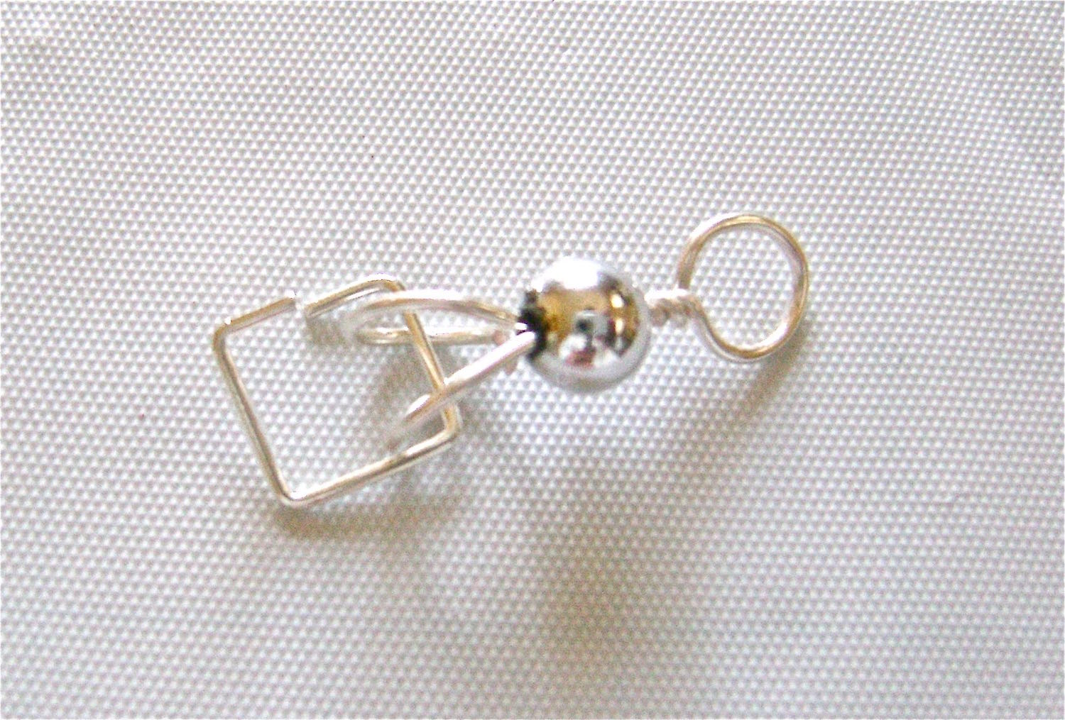 step 6 - Open the metal square by holding one end with pliers and pushing the other end away from you. Create an opening large enough to accommodate the turquoise tube. Slip the square through the two loops.