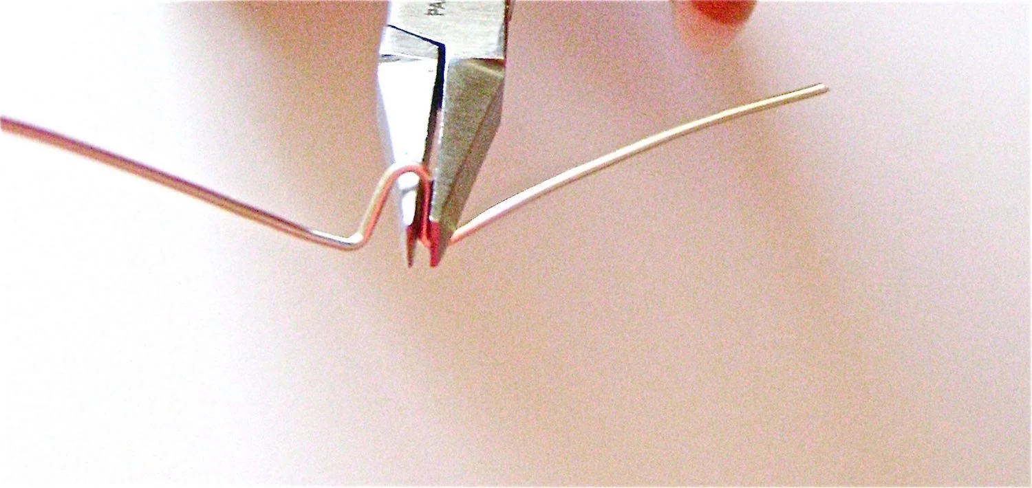 step 1 - To create the earring frame cut the 18 gauge wire to measure 2.5”. Make a center loop by placing a thin round object in the center of the wire and bending the ends together. Push the sharp edge of flat nose pliers into the loop and bend both wires into 90 degree angles.