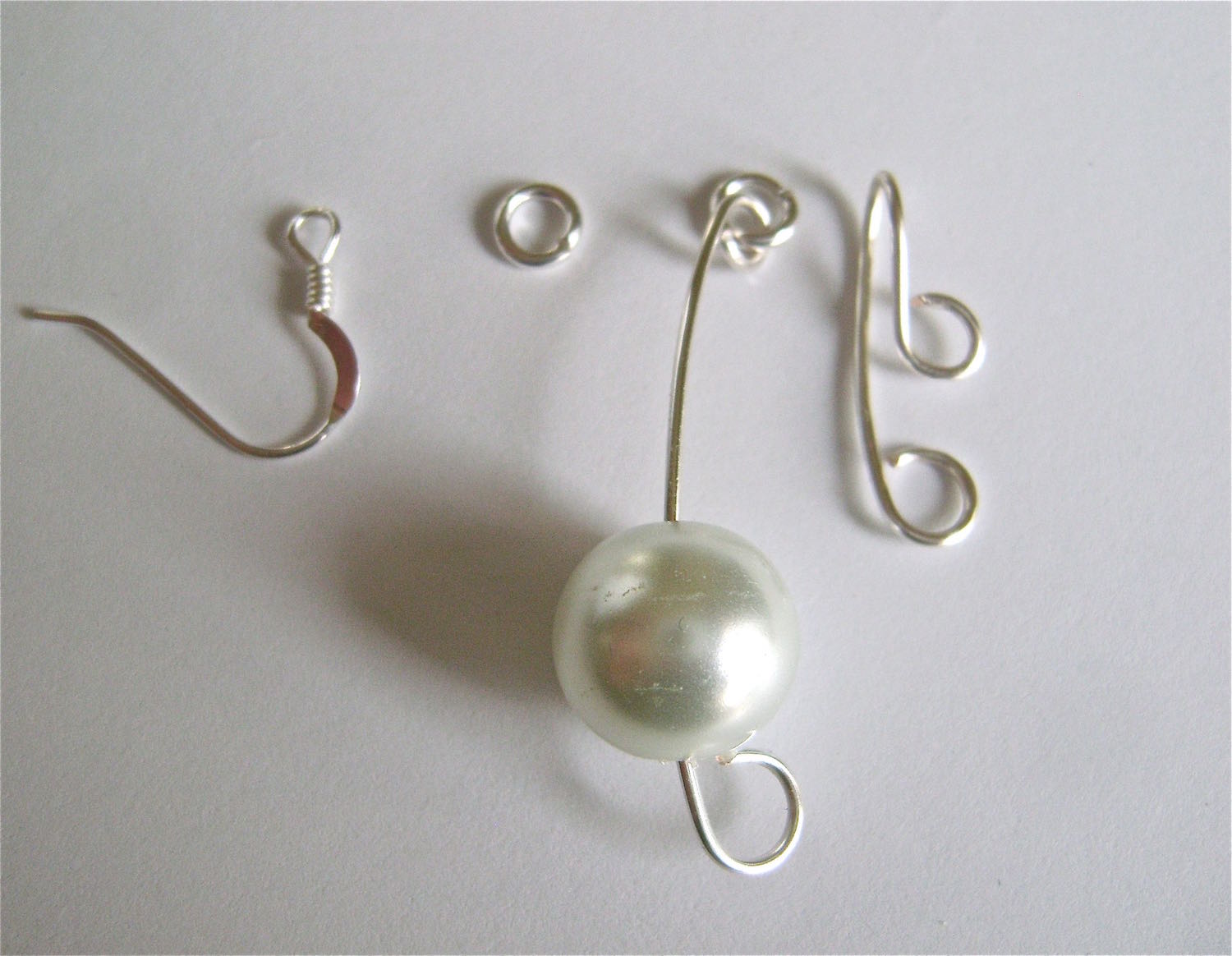 step 5 - Assemble the earring. Insert a 7mm jump ring into the four components in the order pictured above: earring wire, 5mm jump ring, jump ring attached to the pearl wire, and the double curled, folded wire. Wear this earring in the left ear.
