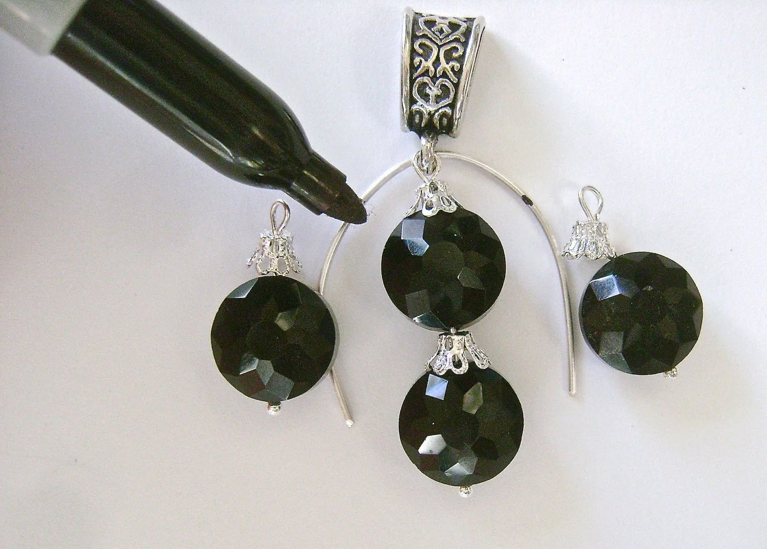 step 4 - Cut a 3” piece of 18 gauge wire. Curve the wire over a round object. Slip the wire through the loop in the bail. On the work surface, position all the beads as they will be in the finished earring. The vertical center of the side beads should be aligned between the two bead centerpiece. Make a mark with a Sharpie indicating where the side bead loops will attach to the wire.