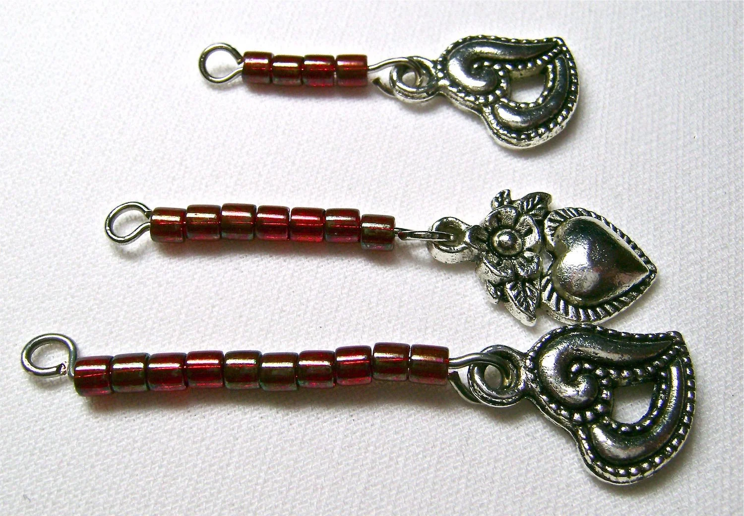 step 8 - Make the dangling heart sections. Cut three pieces of wire, one to measure 1.75”, 1.50”, and 1.25”. Create them the same way you did the connectors except you will attach a small heart to one loop of the wire. The shortest wire section will hold four beads, the next will hold seven beads, and the longest will hold ten beads. (Note that the length of these sections hangs below the one-inch long central heart. If you use a heart longer or shorter than one inch, the length of your sections may need to be adjusted.) 