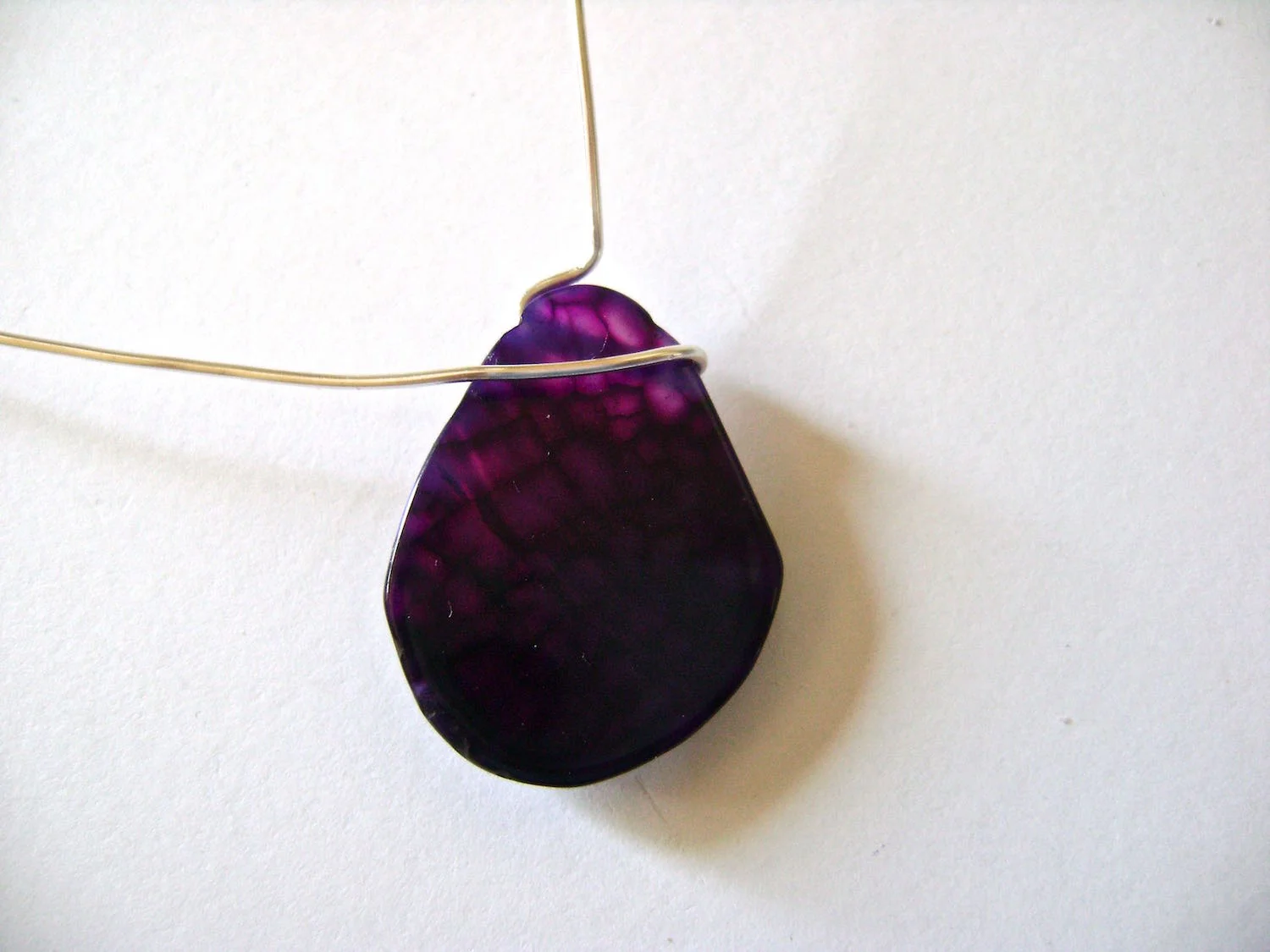 step 9 - Create a bend in the short wire pushing it up against the side of the stone. Make a 90 degree angle in it at the vertical center of the stone. The short end should be facing straight up. Bend the long wire across the upper front of the stone.