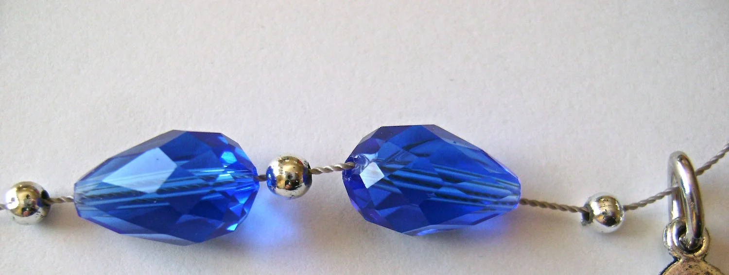 step 5 - Add a small silver bead to the cord followed by the small end of a sapphire bead, a silver bead, the wide end of a sapphire bead, a silver bead, and the link attached to the leaf. This is the center of your necklace.