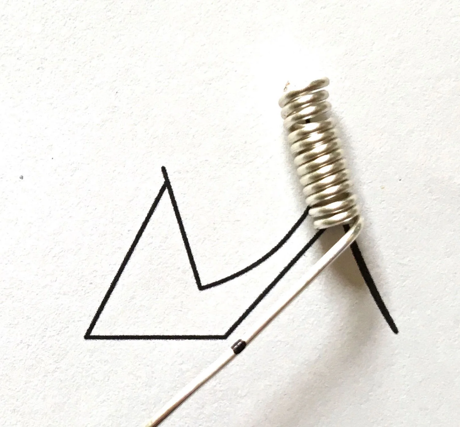 step 1 - Print out the template on paper. Cut an 18 gauge wire to measure 9.50”. Wrap the wire around a knitting needle or other tube 12 times. The tube thickness should be no less than that of two pieces of wire side by side. Position the coil on the paper and mark the first bend on the wire.